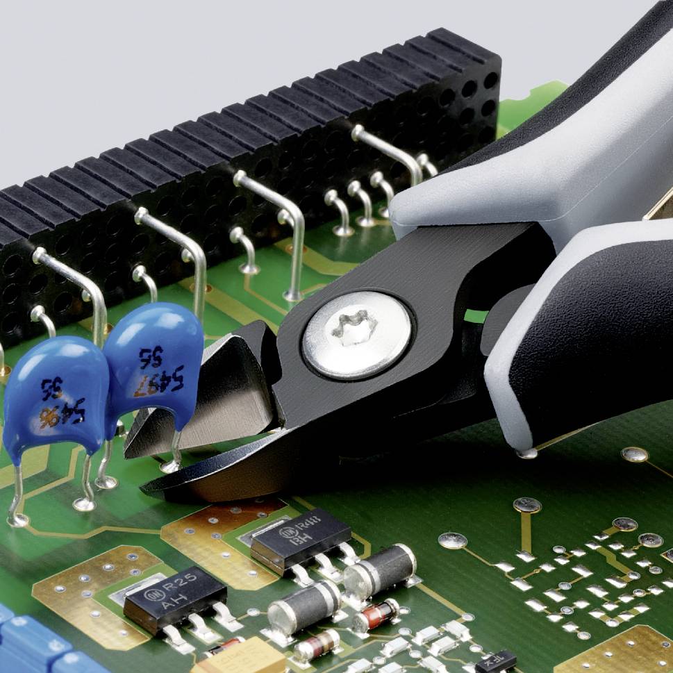 Kleště řezají drát na elektronické desce s modrými kondenzátory a černými čipy, s důrazem na přesnost a techniku.