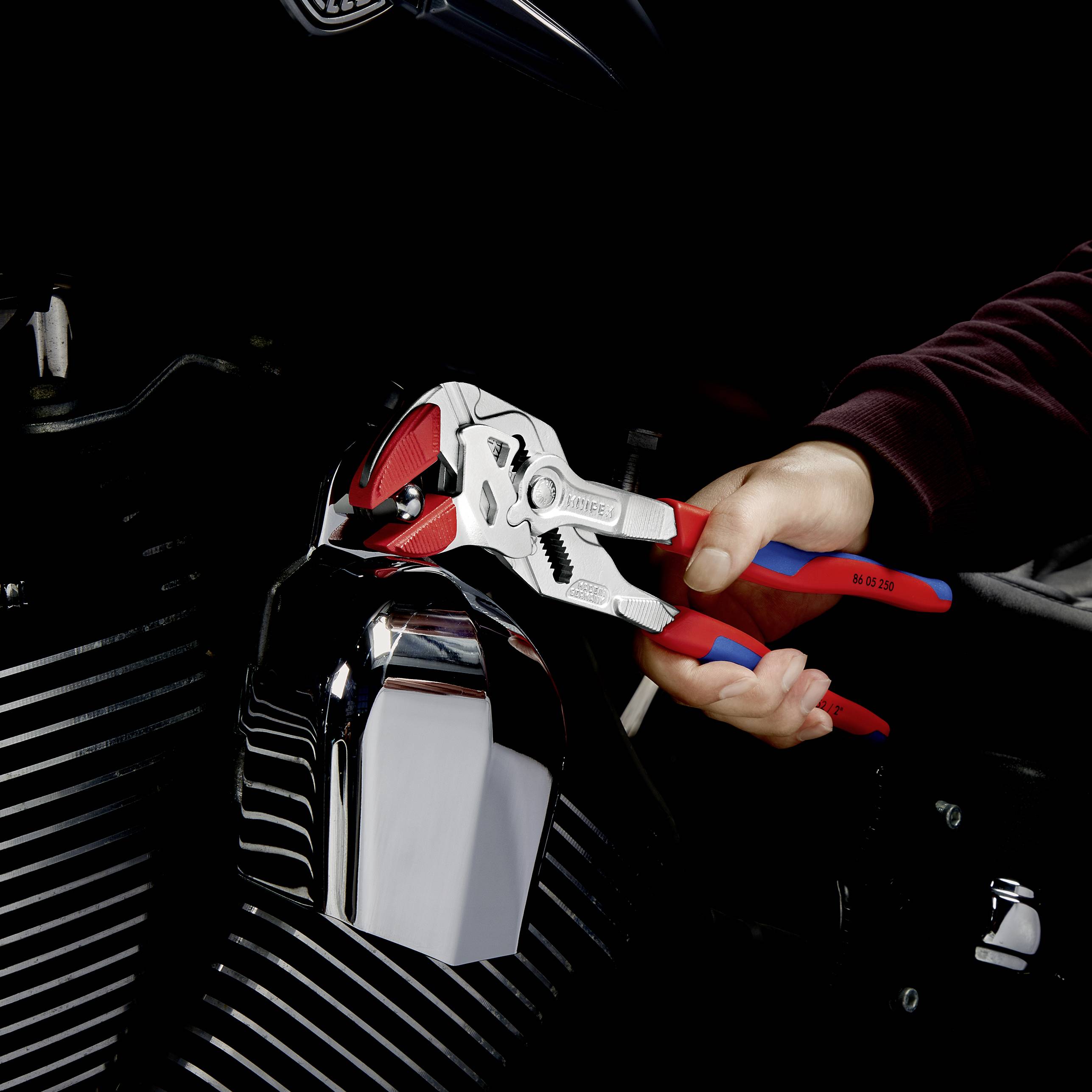 Jedna ruka drží nastavitelné kleště, zatímco pracuje na motoru motocyklu. Kleště jsou otevřené a zachycují kovový povrch.