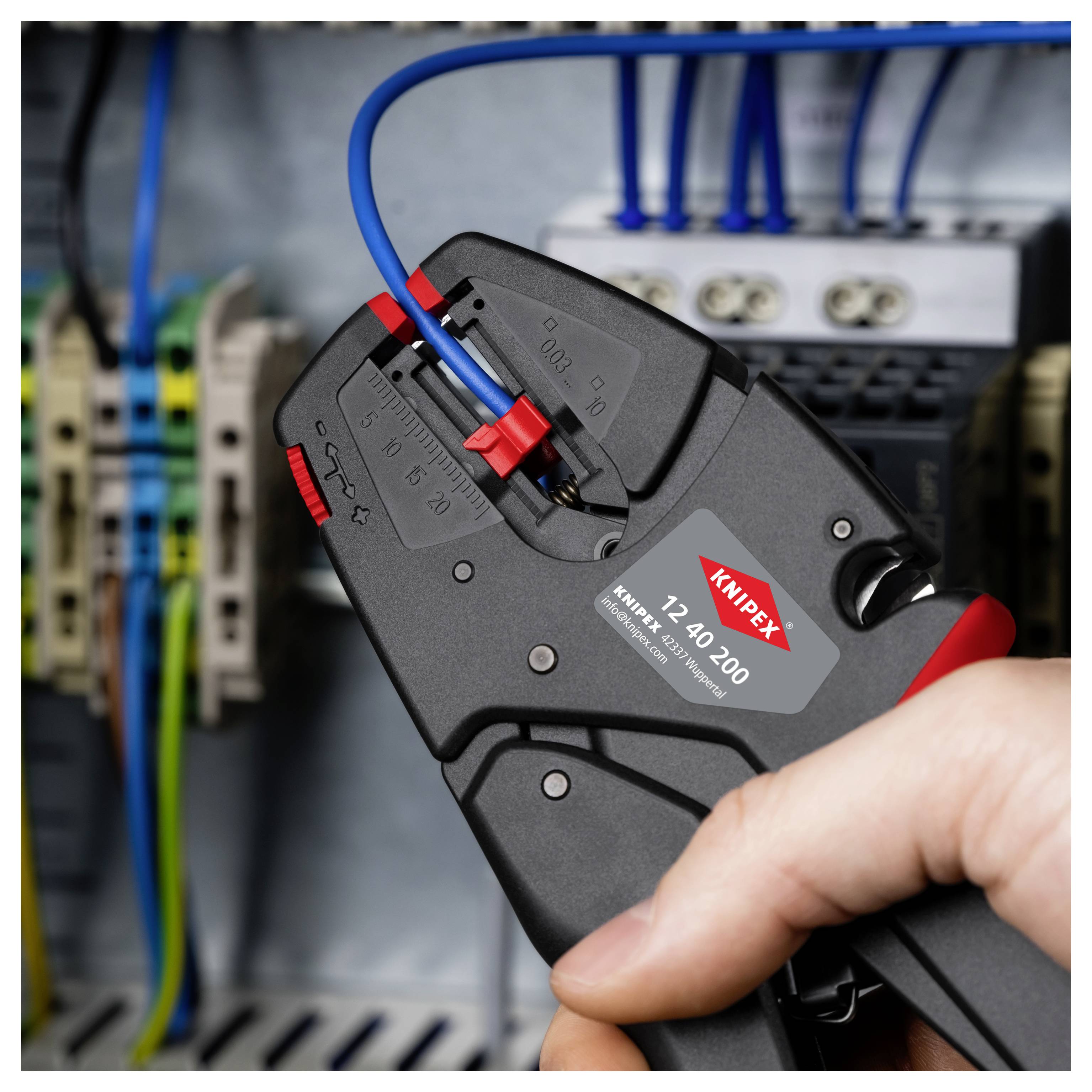 Ruka používá krimpovací nástroj k připojení modrého vodiče v elektrickém rozvaděči, což demonstruje elektrikářskou práci a funkčnost nástroje.