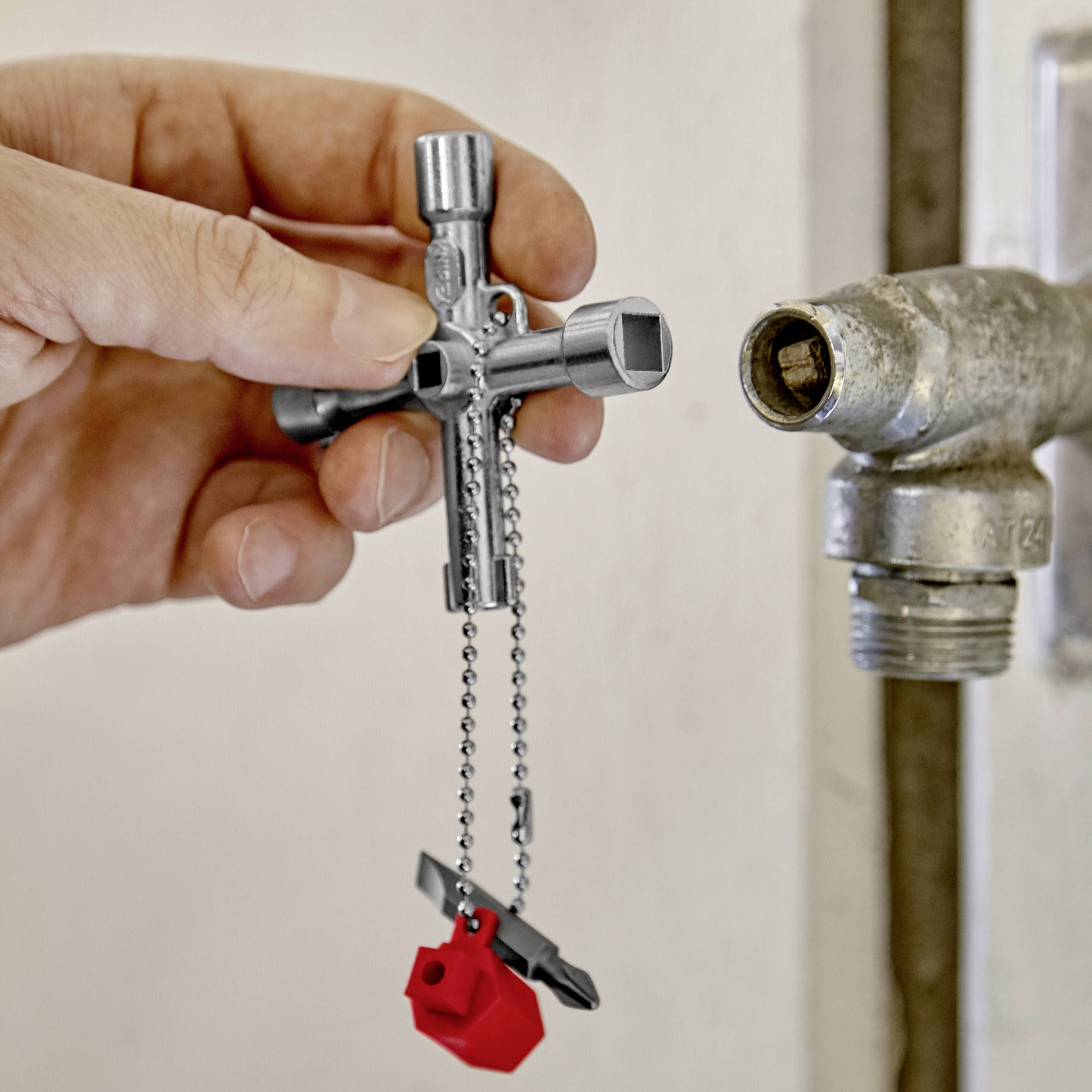 Ruka držící křížový klíč na vodovodní ventil. Klíč má tvar klíče a visí na řetízku připevněném k lego kostce.