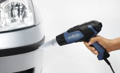 Jedna ruka drží horkovzdušnou pistoli u rohu automobilu, pravděpodobně za účelem zahřátí nebo opravy dané oblasti.