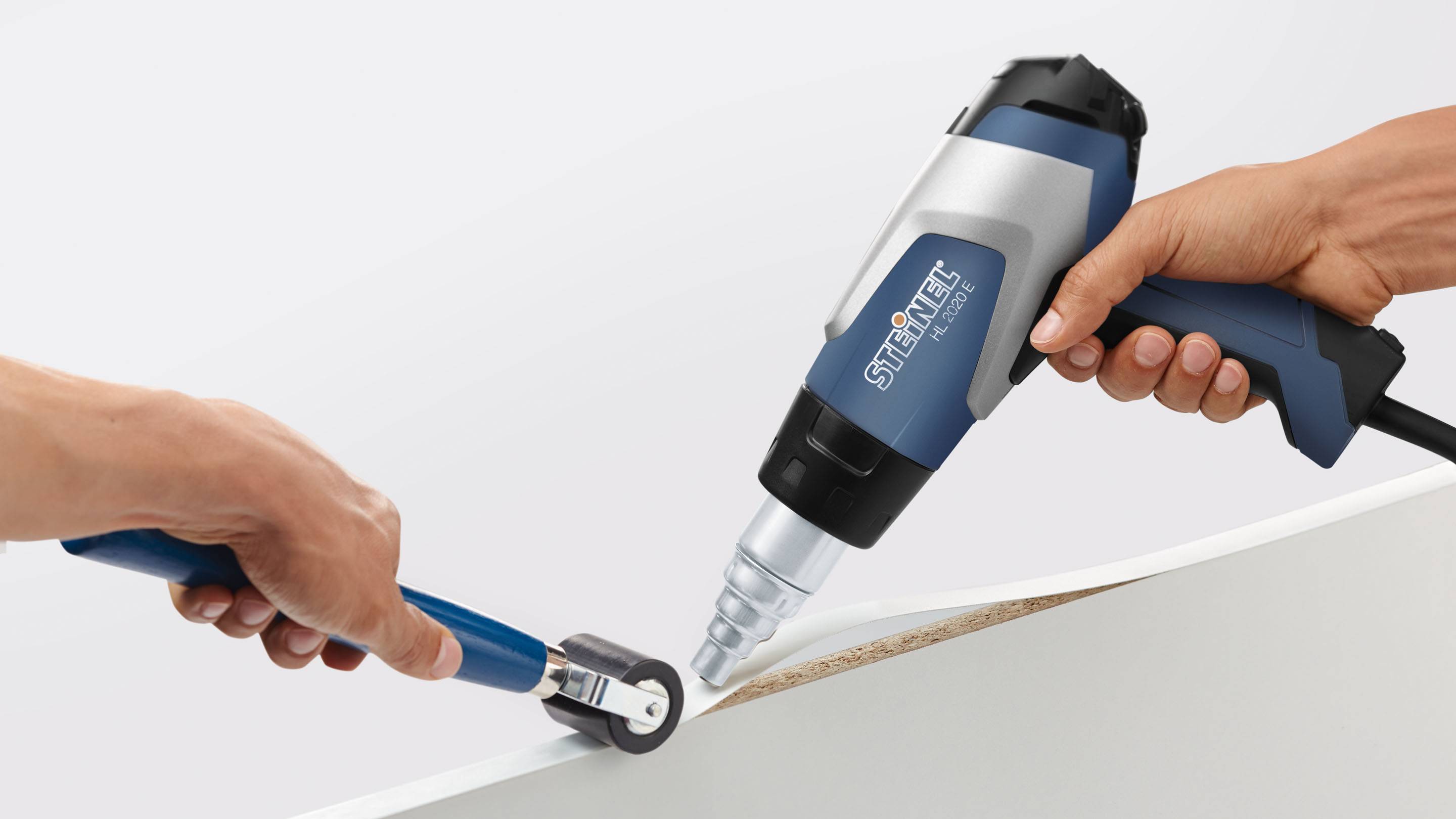 Jedna osoba používá horkovzdušný ventilátor a stěrku k upevnění hrany pásky na desku.