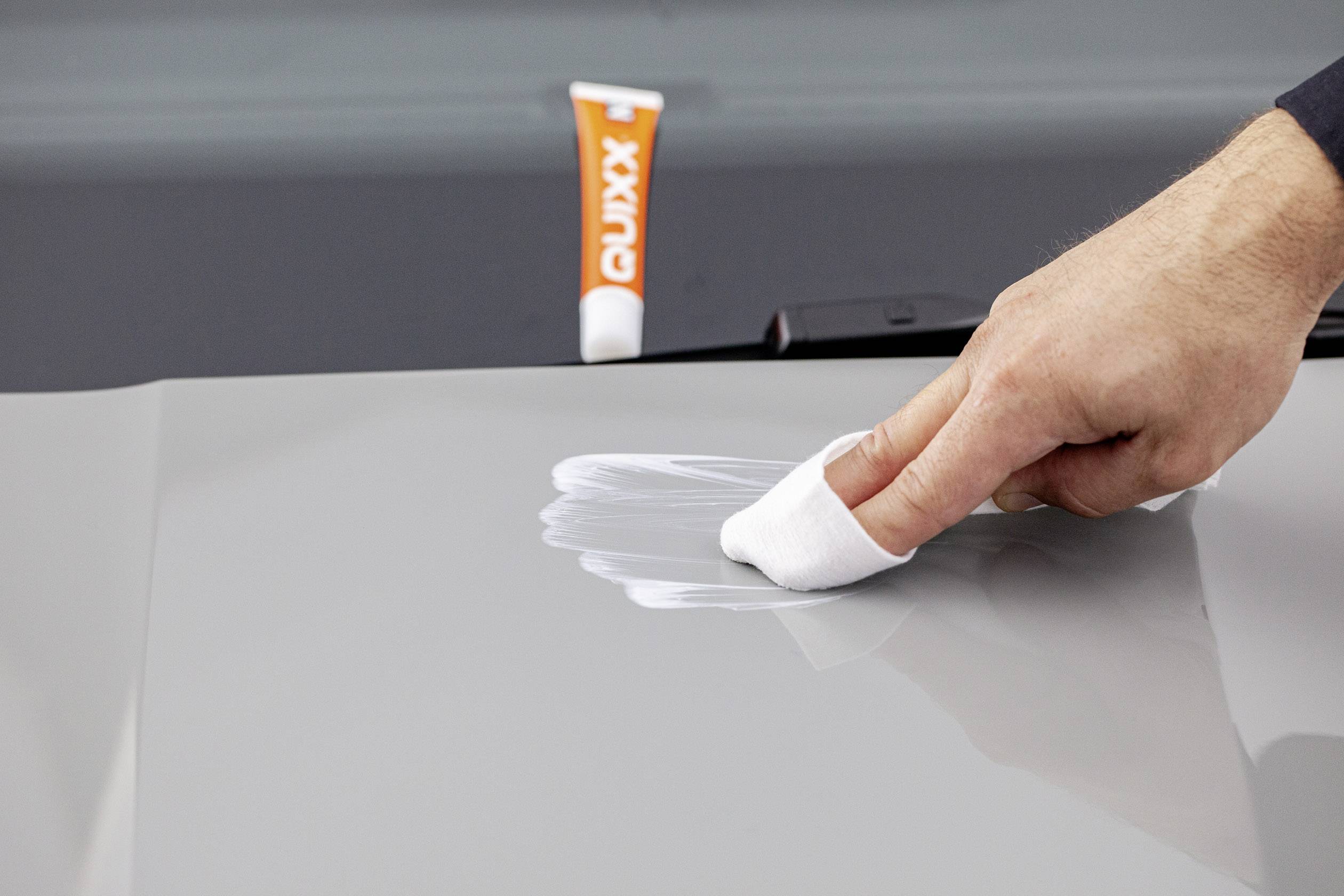 Ruka leští autolak bílou utěrkou, v pozadí je umístěna tuba autokosmetiky.