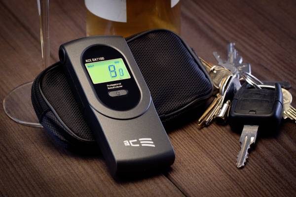 Digitální alkoholový tester zobrazující '0.8' leží vedle svazku klíčů na dřevěné podložce.