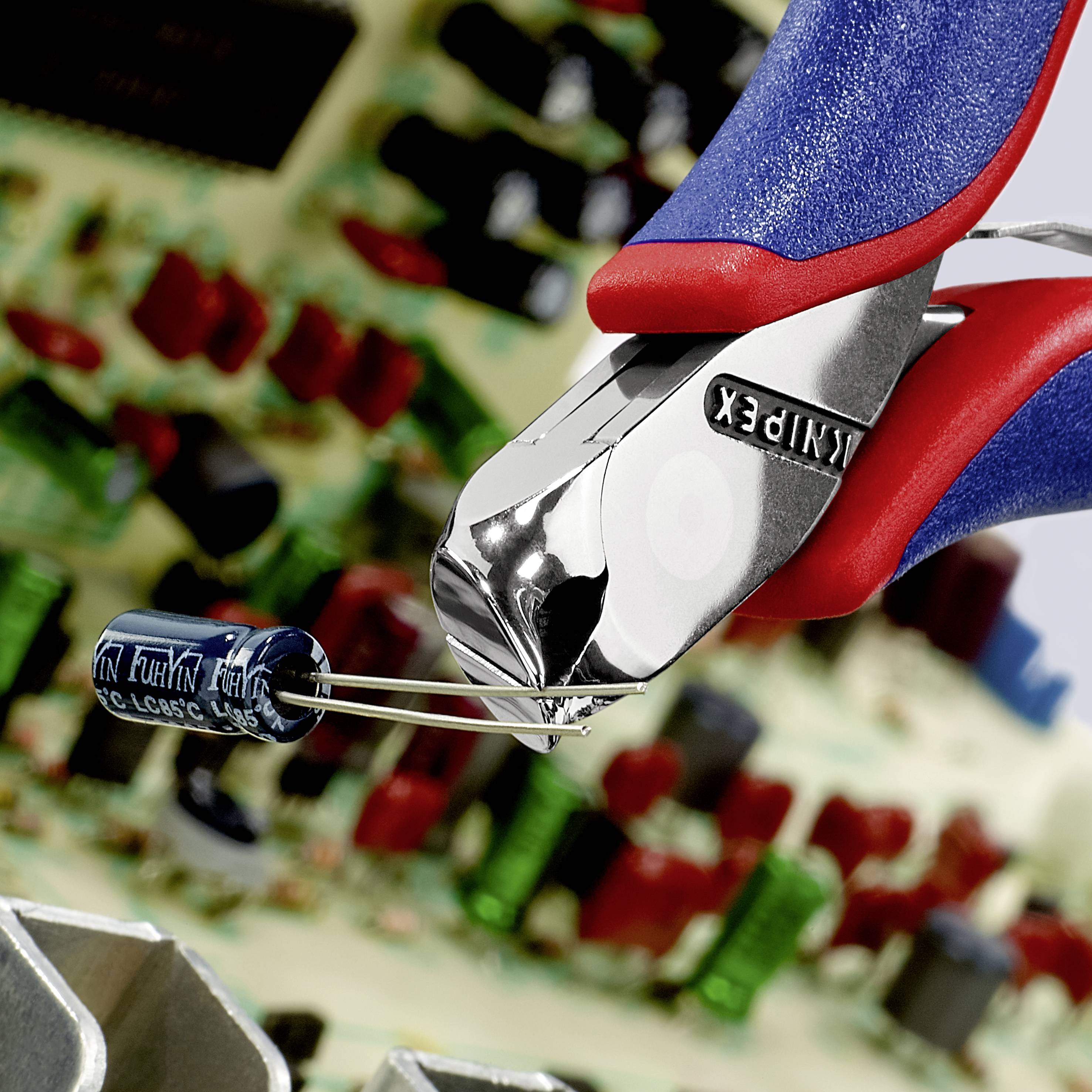 Kleště drží modrý kondenzátor nad deskou plošných spojů s elektronickými komponenty. V pozadí rozmazané elektronické obvody.