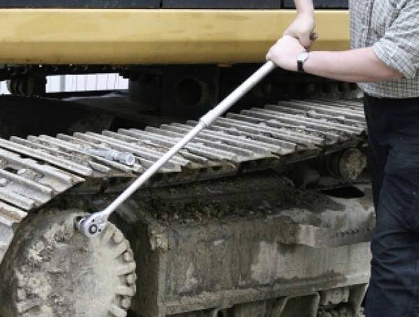 Osoba používá dlouhý klíč k utažení šroubů na pásu stavebního stroje, což demonstruje údržbářskou práci.