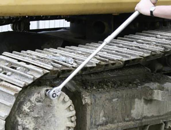 Osoba používá dlouhý klíč k seřízení pásu těžkého stavebního stroje. Zaměření je na údržbové práce prováděné na pásu vozidla.