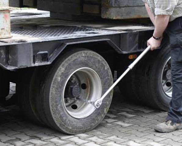 Osoba používá momentový klíč k utažení šroubů na velkém nákladním kole, čímž zajišťuje pevné připevnění.