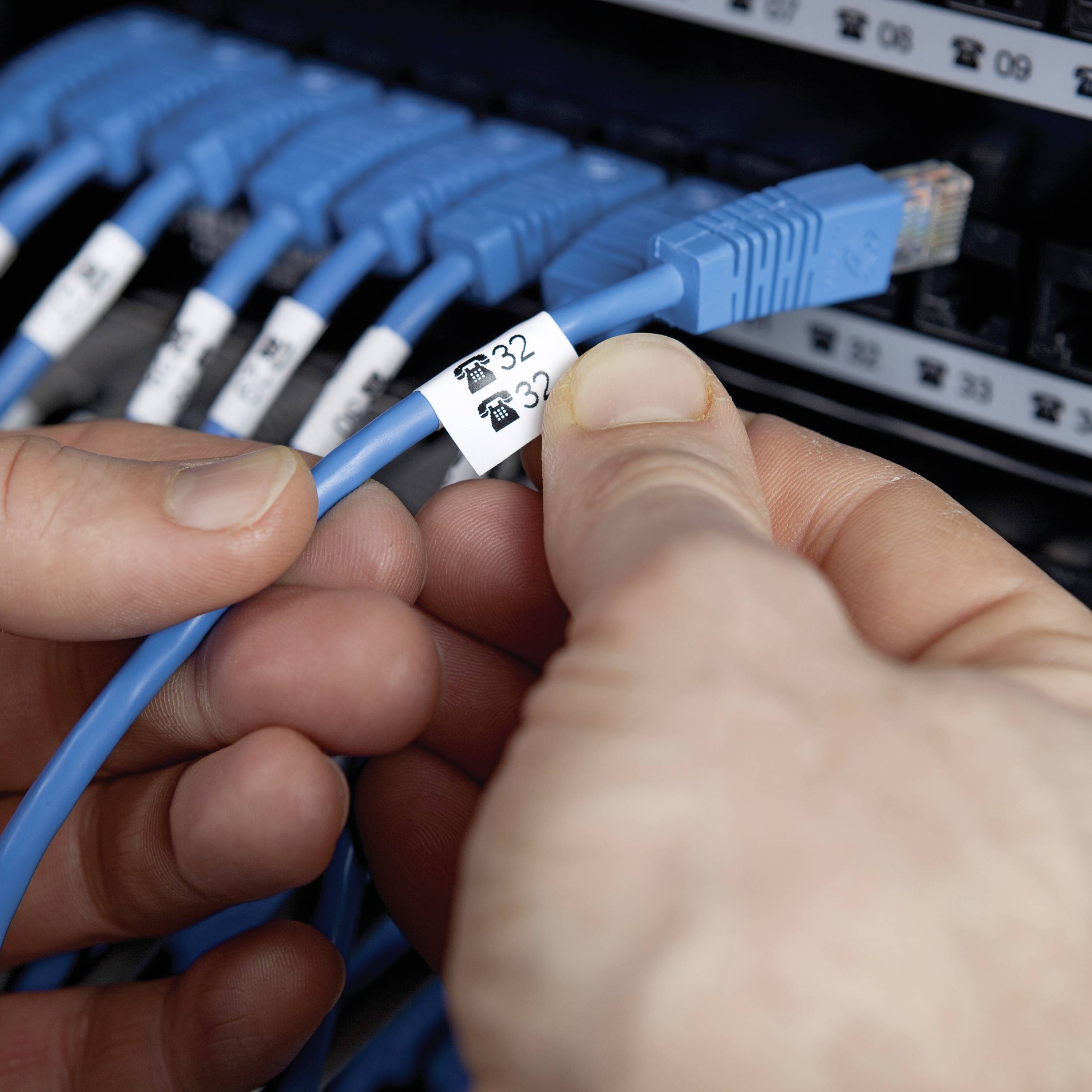 Člověk drží modré síťové ethernetové kabely s nápisem „32" před stojanem se serverem. Několik modrých kabelů je připojeno.