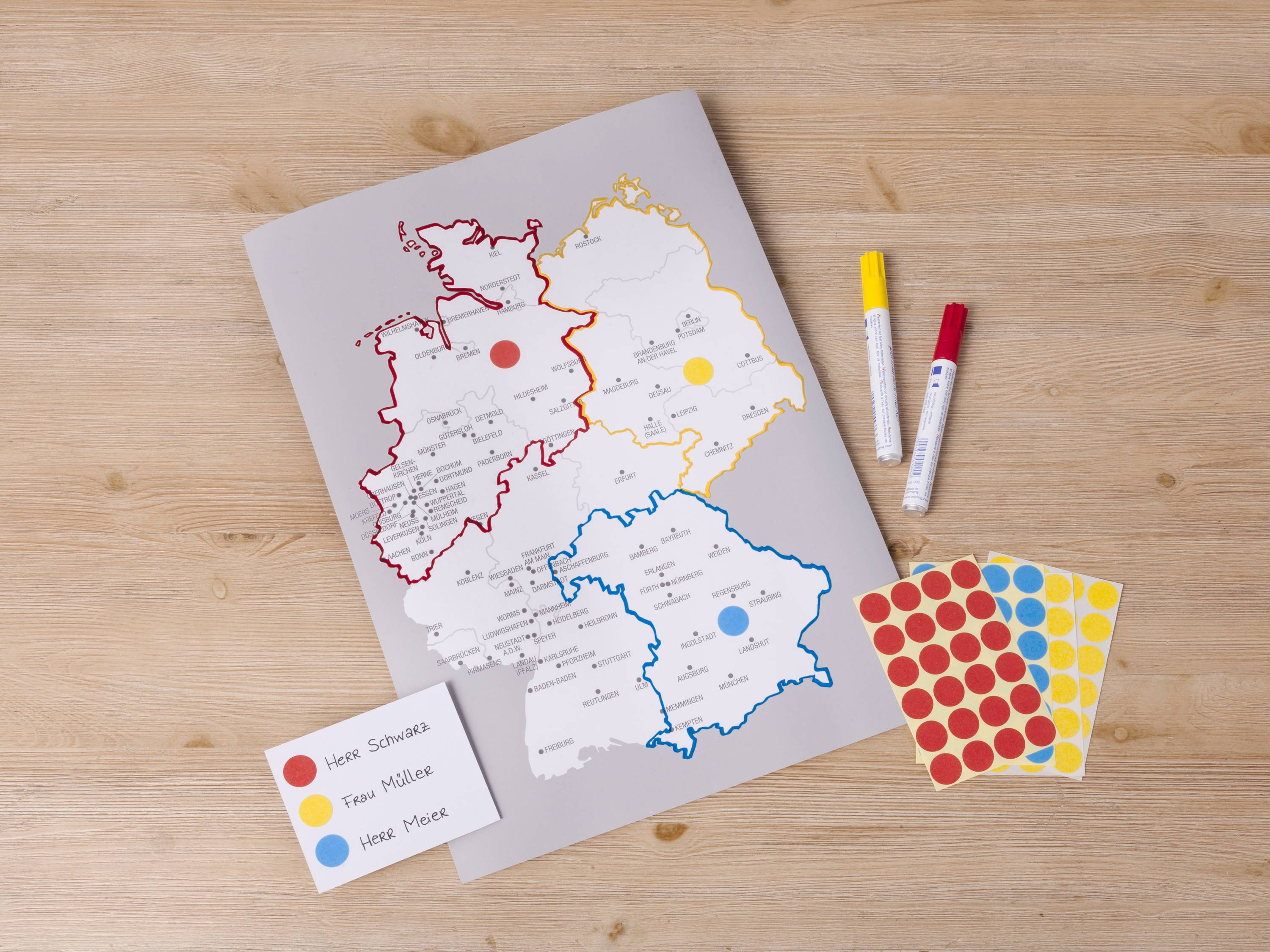Mapa s barevnými regiony, červenými a žlutými značkami. Vedle leží samolepky a fixy. Hlavní oblasti mapy jsou označeny červeně, modře a žlutě.