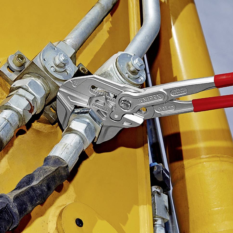 Instalatérské kleště zasahují do kovového šroubení na žlutém hydraulickém systému. Nástroj a komponenty v centru pozornosti, demonstrace technického použití.