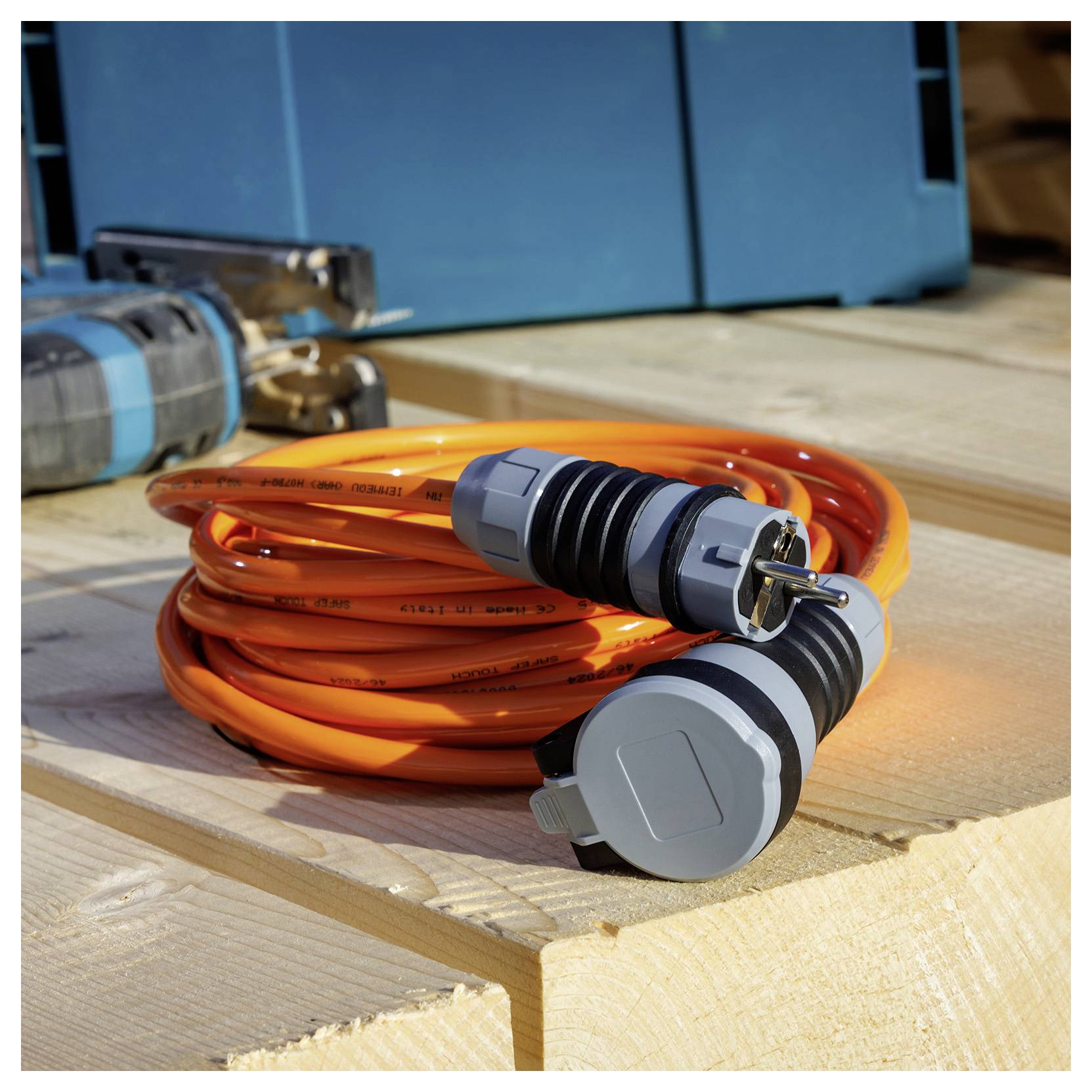 Svitnutý oranžový elektrický kabel se dvěma šedými konektory ležící na dřevěné ploše venku.