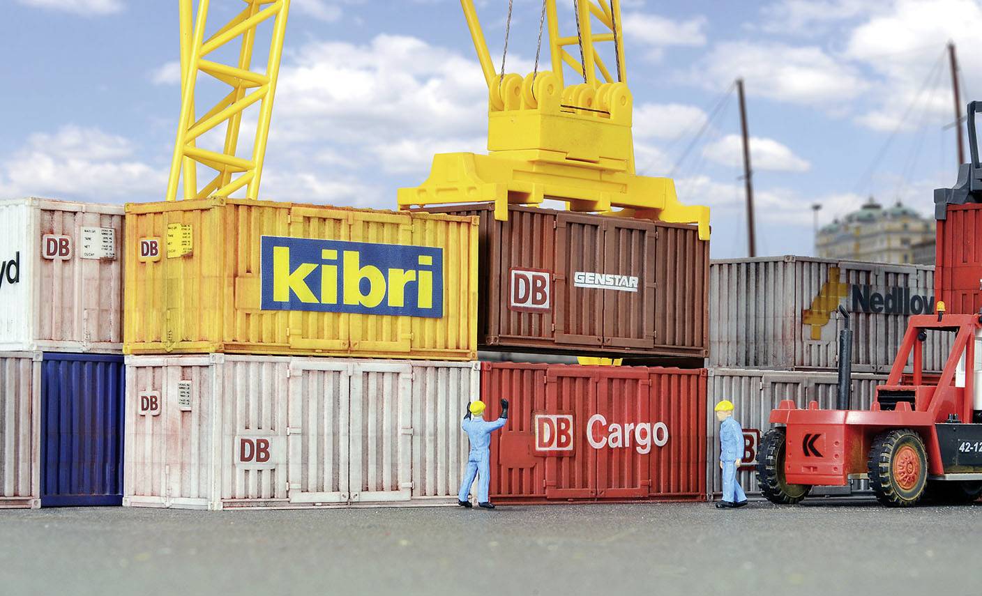 Dva dělníci v přístavu přemisťují kontejnery pomocí jeřábu. Kontejnery jsou označeny nápisy 'DB Cargo' a 'kibri'. Vedle stojí vysokozdvižný vozík.