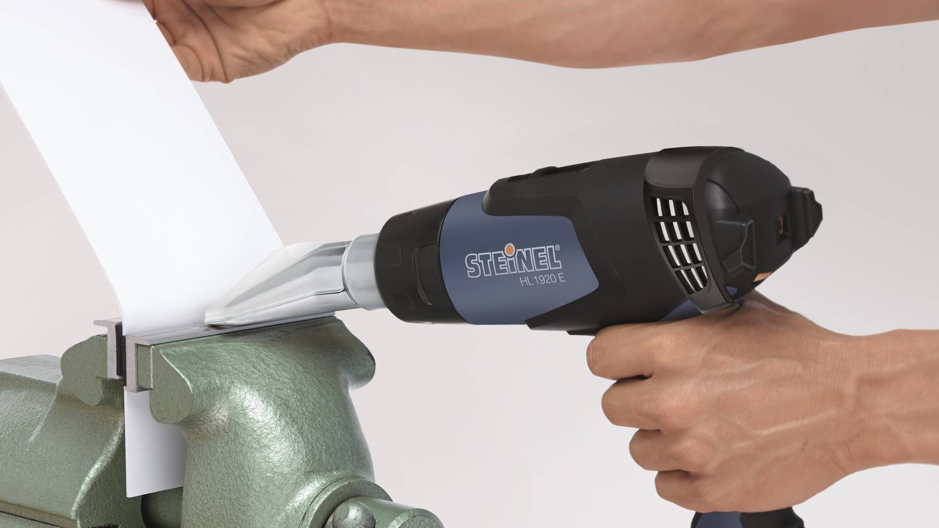 Osoba používá horkovzdušnou pistoli k tvarování nebo opracování bílého plastu na hraně kovového obrobku.