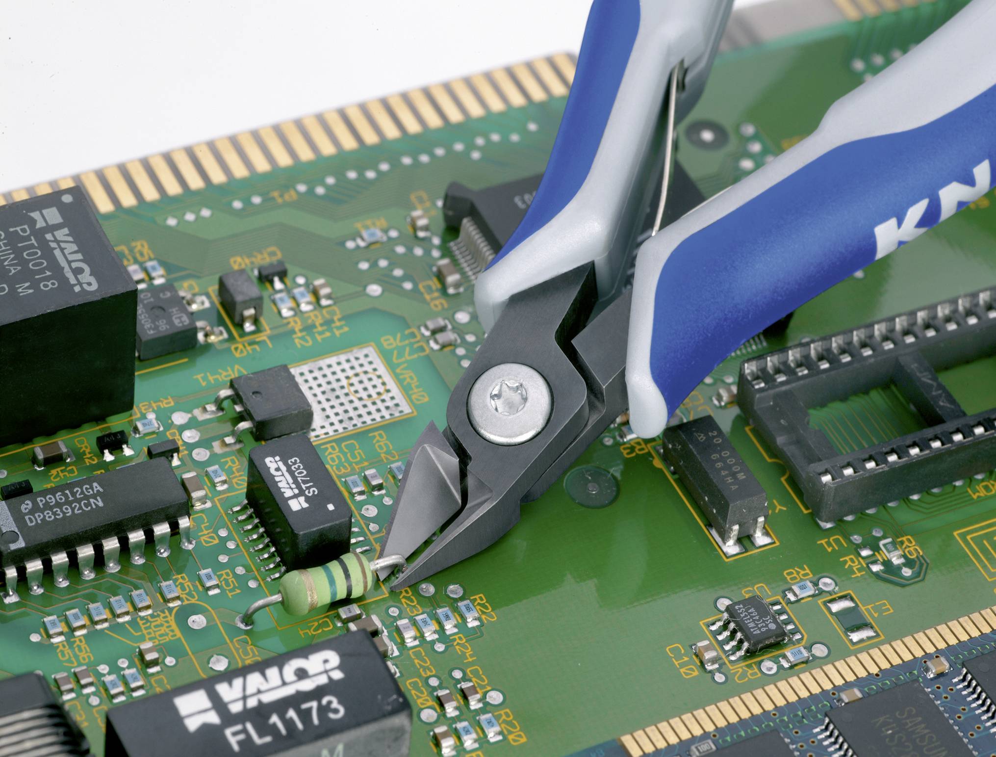 Modrá kleště rozřezávají zelený odpor na desce plošných spojů osazené čipy a elektronickými komponenty.