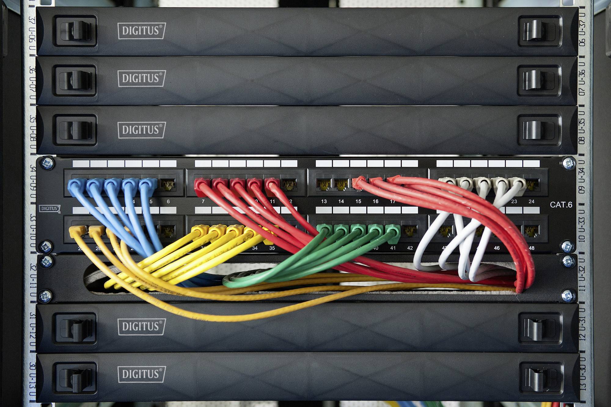 Síťová rozvodná skříň s několika síťovými switchi je zobrazena. Barevné ethernetové kabely jsou zapojeny a propojeny.