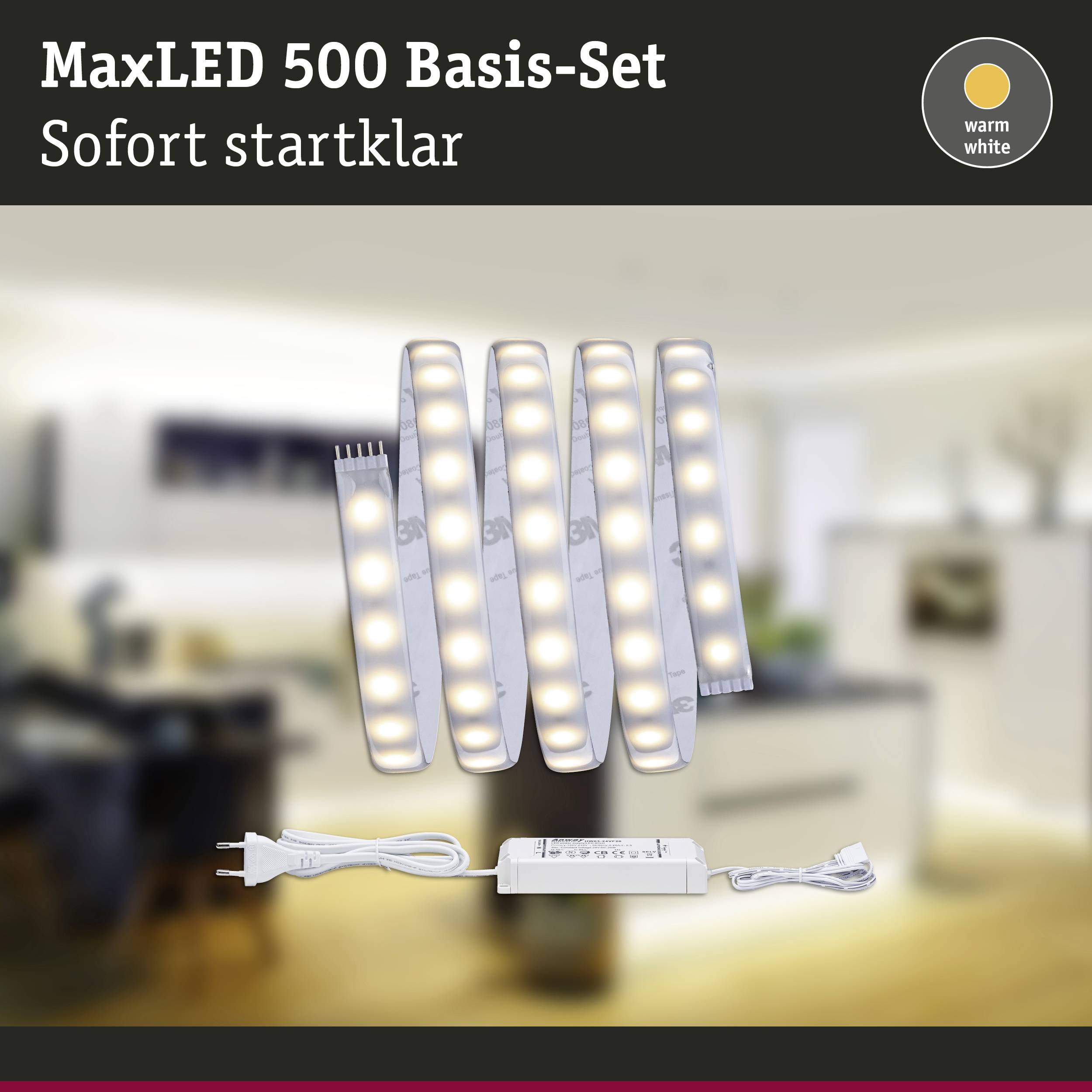 Sada 'MaxLED 500 Basis-Set' s LED osvětlením, okamžitě připravená k použití. Pozadí zobrazuje rozmazaný obývací pokoj, text uvádí 'teplá bílá'.