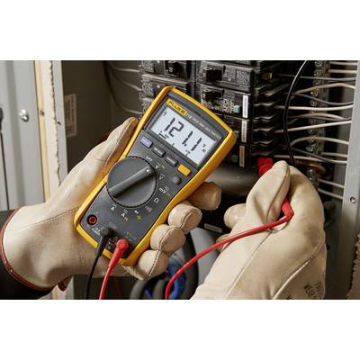 Jedna osoba měří digitálním multimetrem napětí 121,1 voltů na elektrickém rozvaděči.