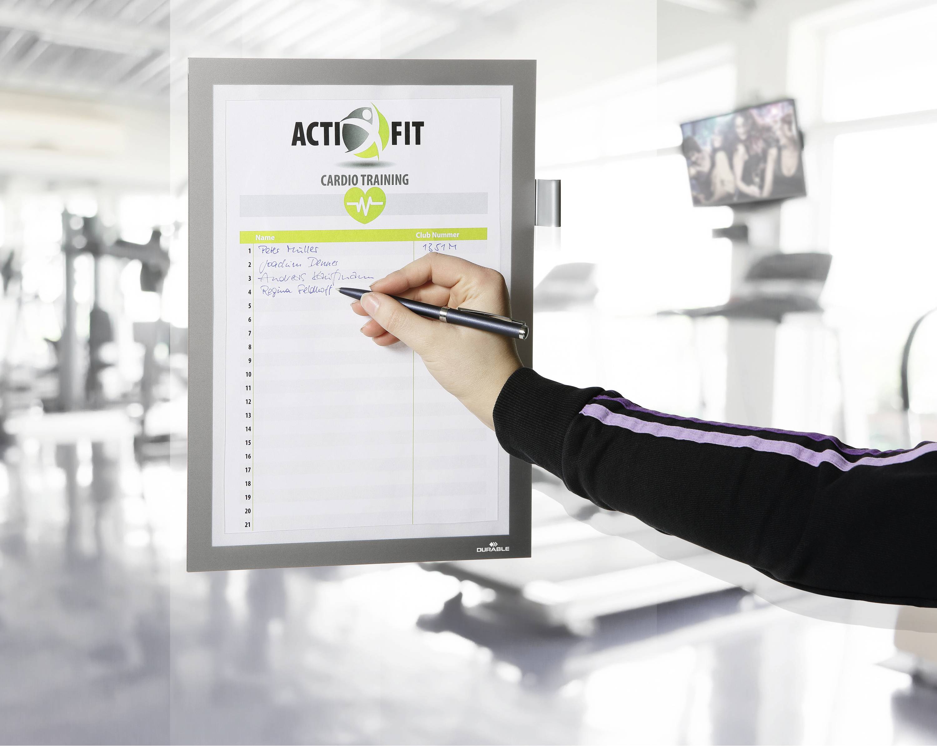Osoba píše perem na formulář s nadpisem 'ACTIFIT Cardio Training' v posilovně.