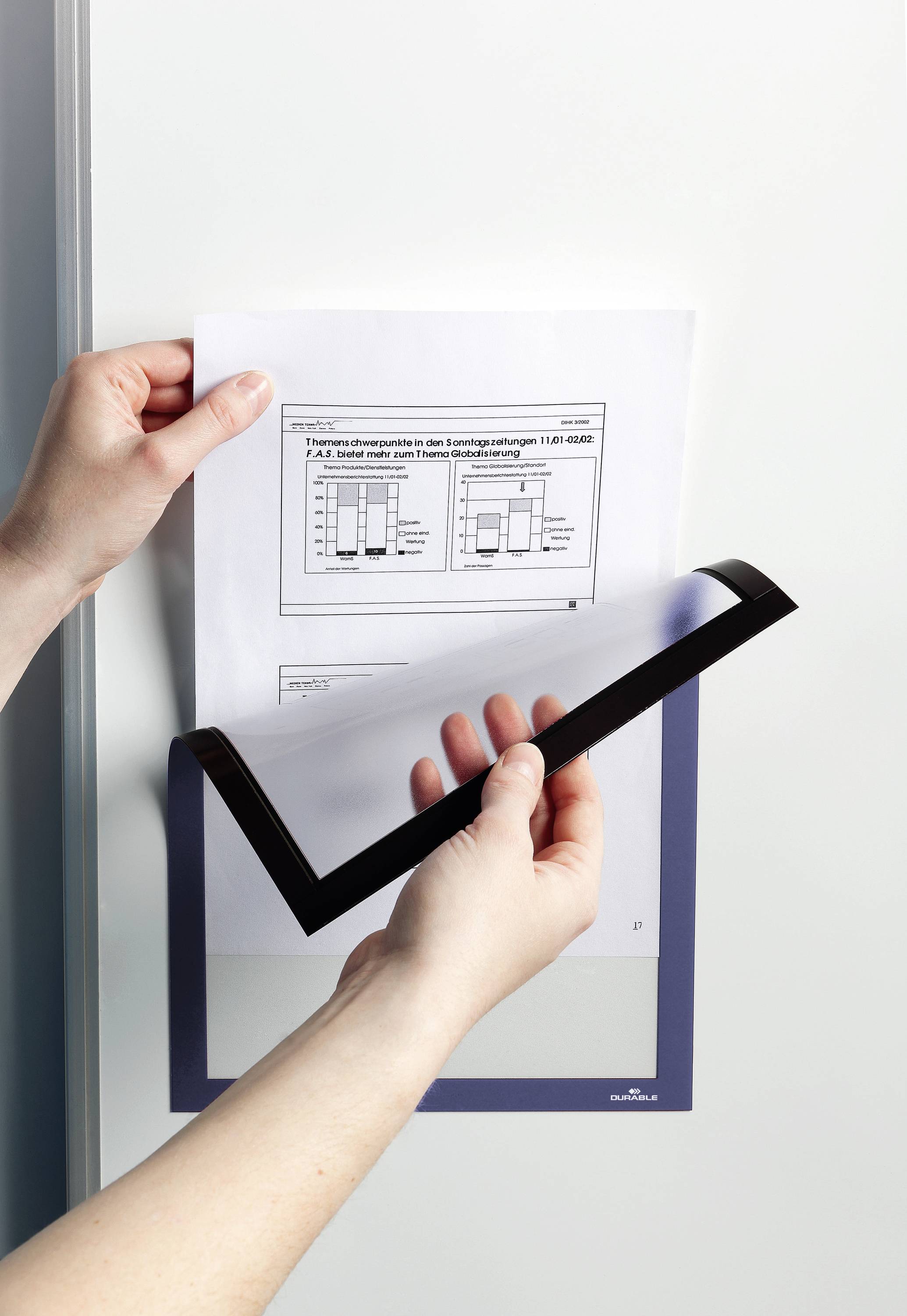 Osoba drží list papíru s diagramy, který je připevněn magnetickým držákem dokumentů k metalické ploše.