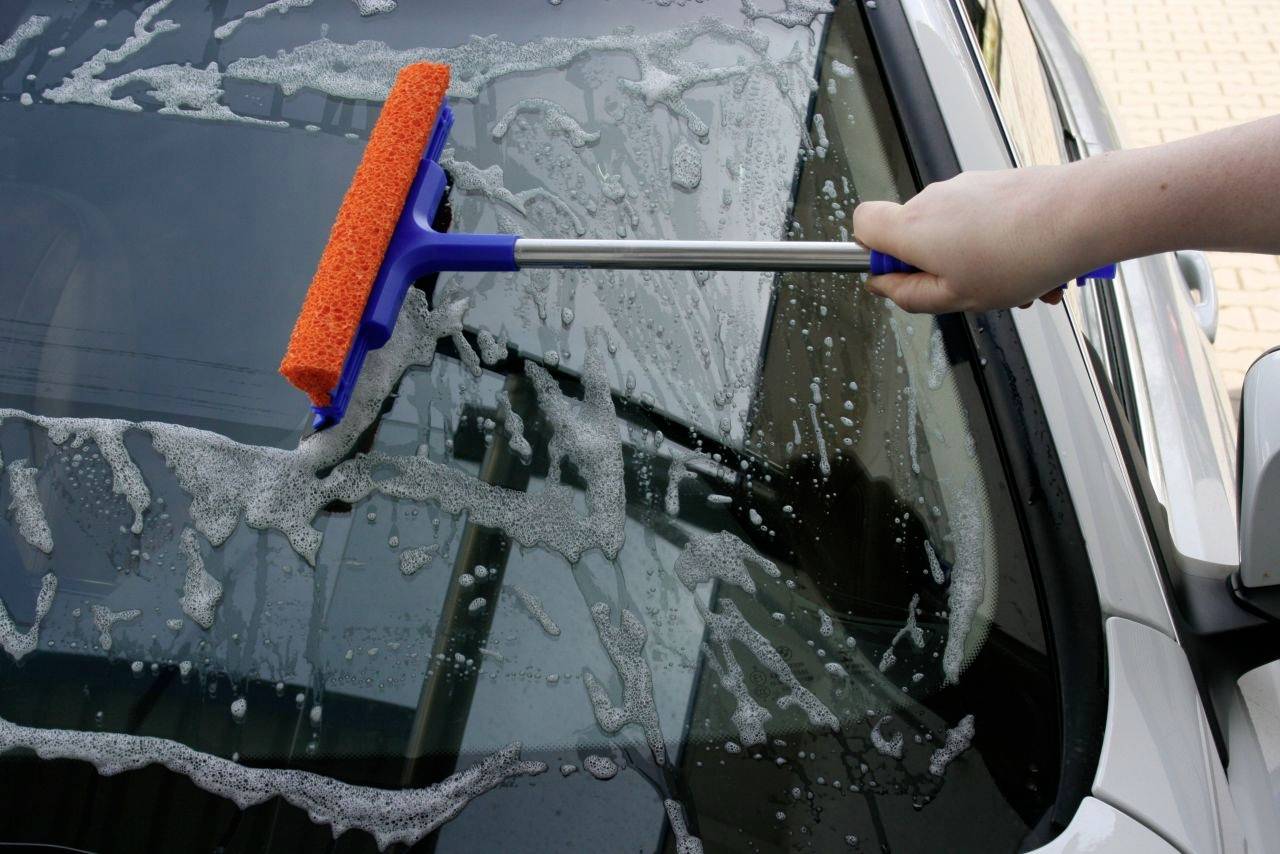 Člověk čistí autosklo stěračem.