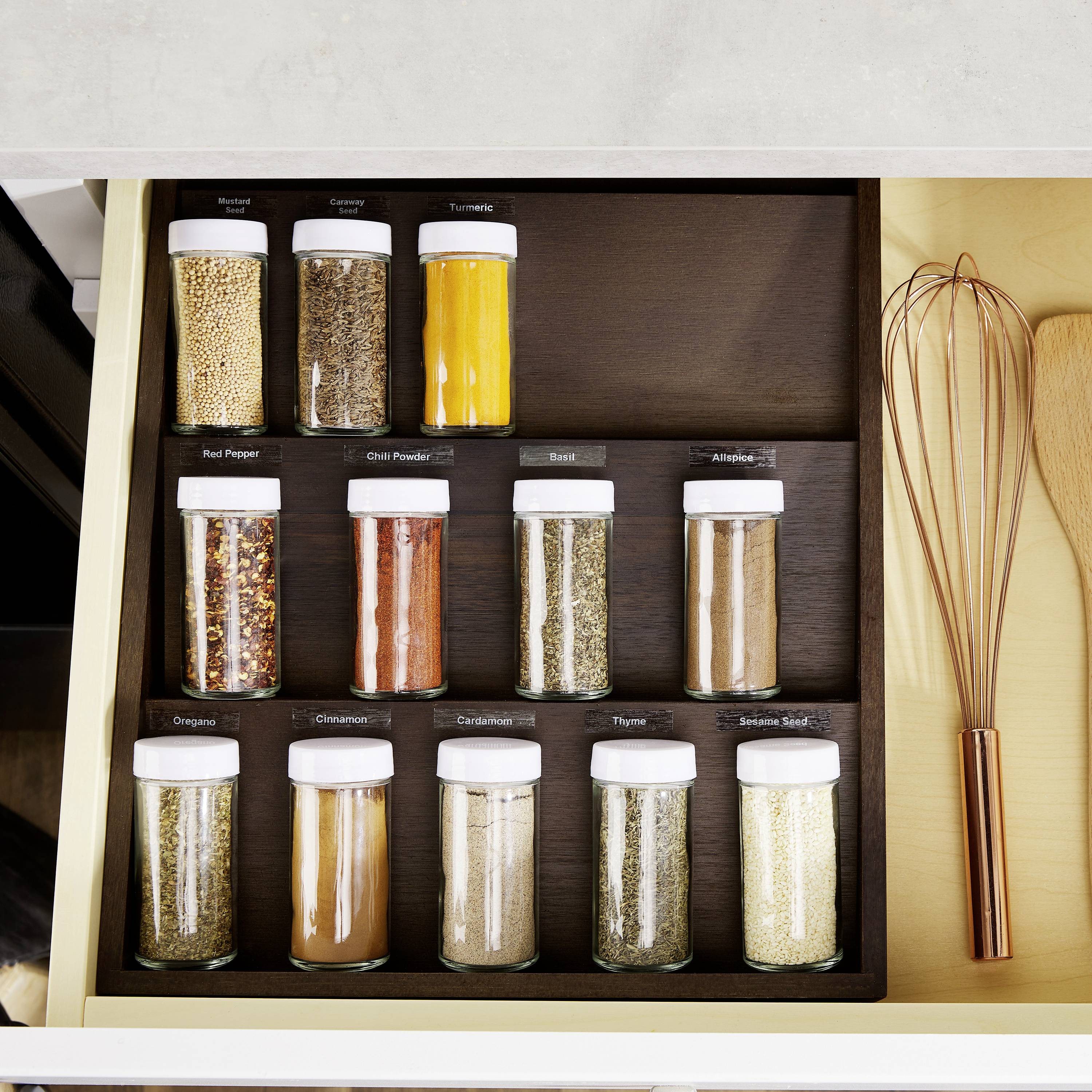 Šuplík na koření s 15 skleničkami: pepř, chilli, bazalka, oregano, skořice. Každá sklenička je označena a pečlivě uspořádána.
