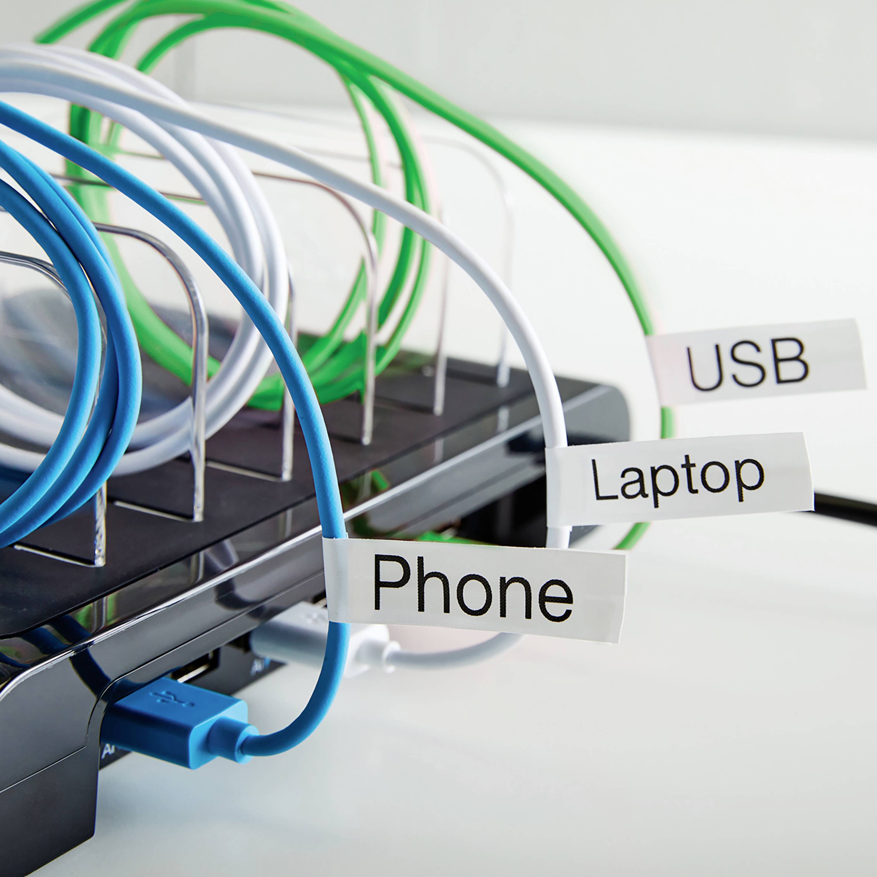 Držák kabelů s modrými, bílými a zelenými kabely, označenými štítky 'Telefon', 'USB' a 'Notebook', organizuje několik nabíječek.