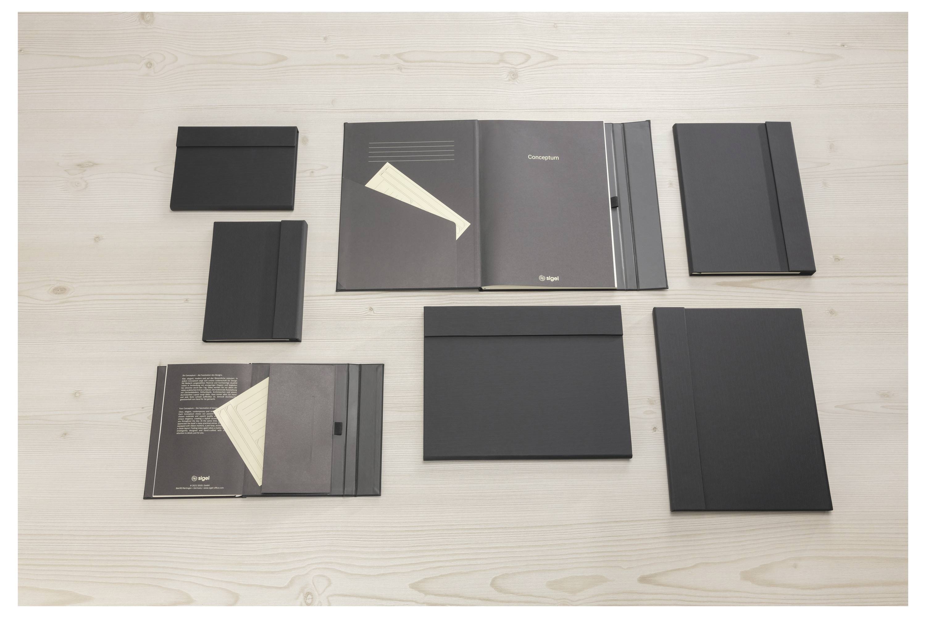 Šest černých prezentačních složek a brožur uspořádaných na světlé dřevěné ploše, ukazujících různé velikosti a designy obálek.