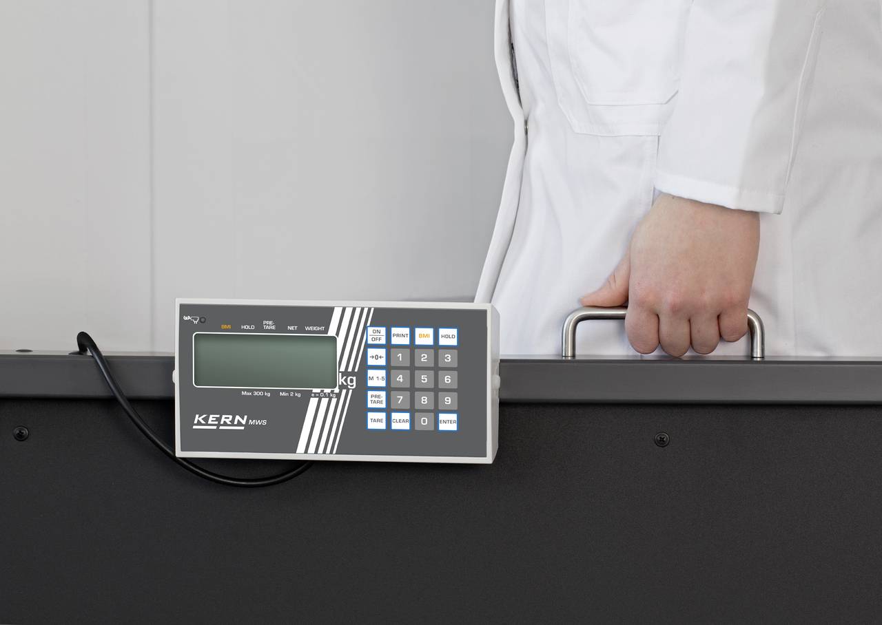 Osoba v bílém laboratorním plášti drží přepravní box s digitálním displejem a numerickou klávesnicí.