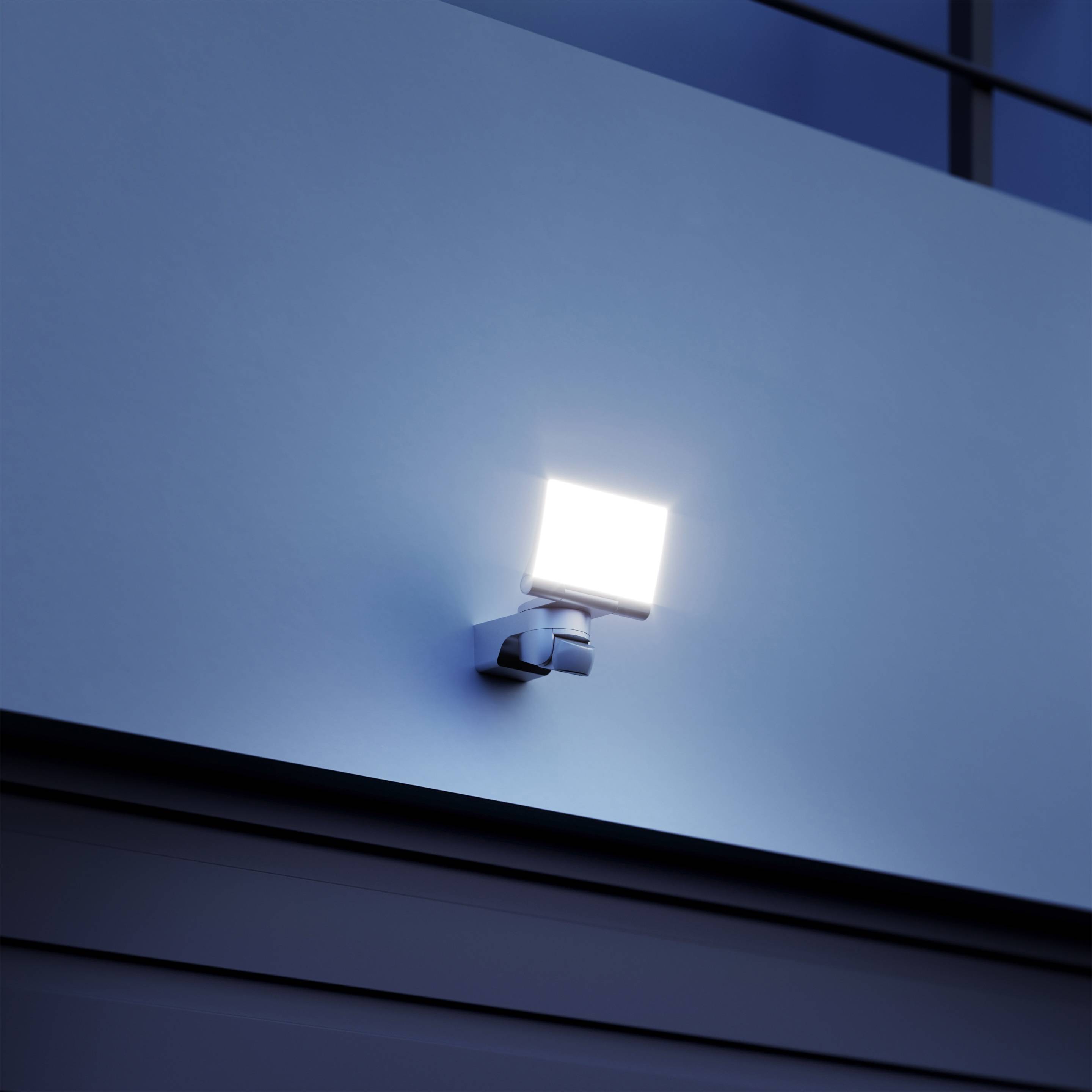 LED nástěnná lampa připevněná k venkovní zdi osvětlující okolí za soumraku.