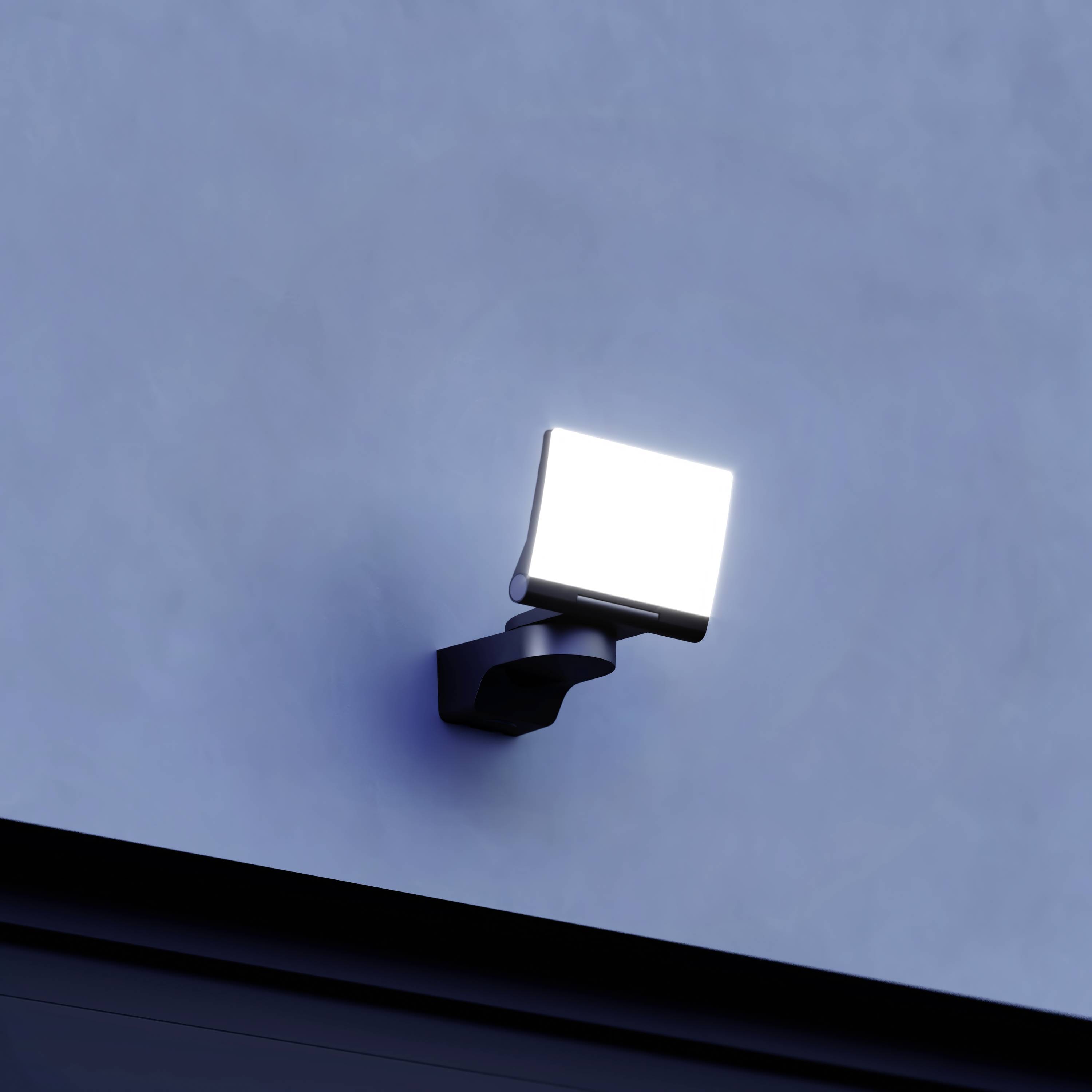 Jasná venkovní lampa je namontována na modré zdi a silně svítí.