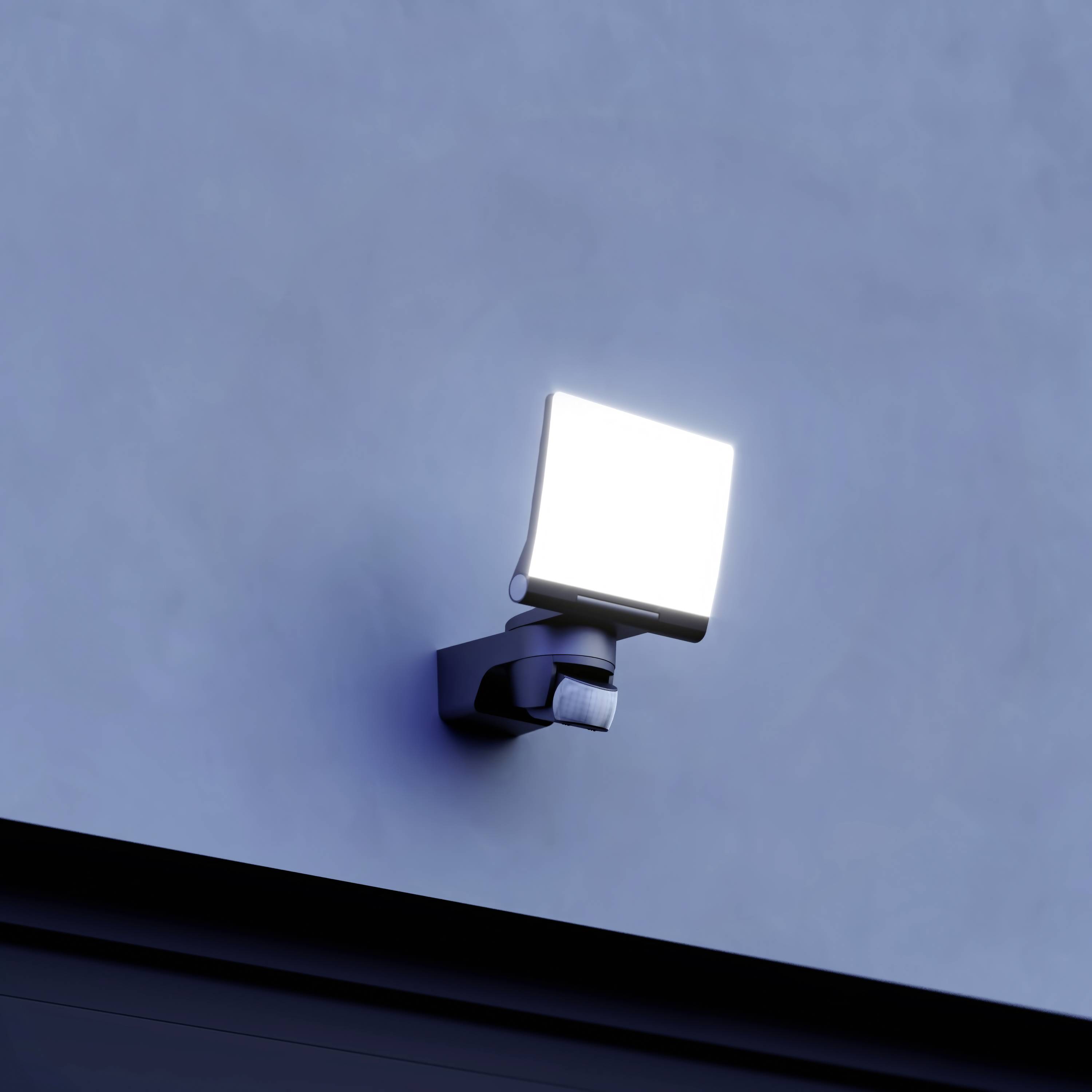 Zářivá venkovní lampa na zdi za soumraku, která osvětluje okolí jasným světlem.