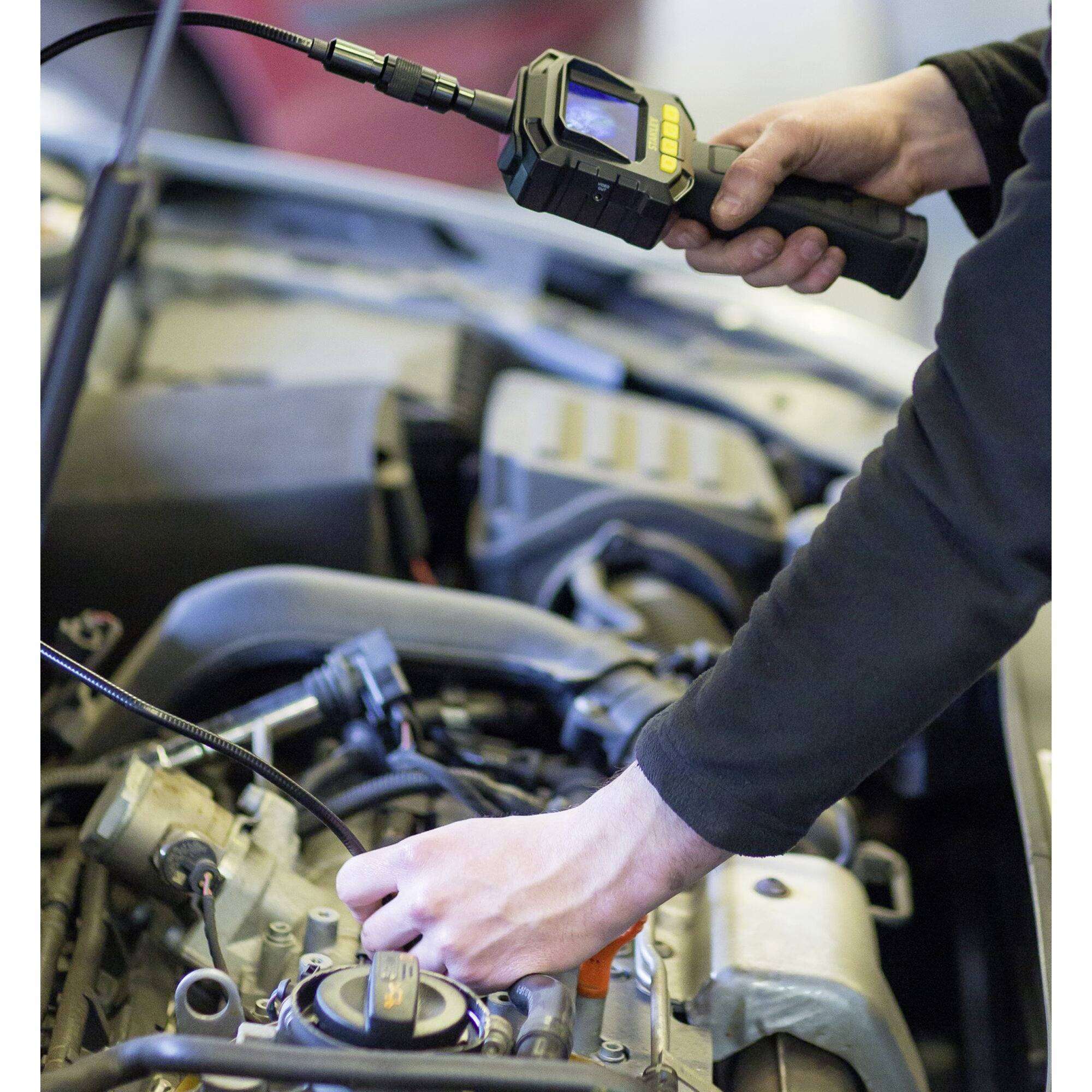 Mechanik používá diagnostický nástroj ke kontrole motoru v autoservisu. Ruce obsluhují přístroj nad otevřeným prostorem motoru.