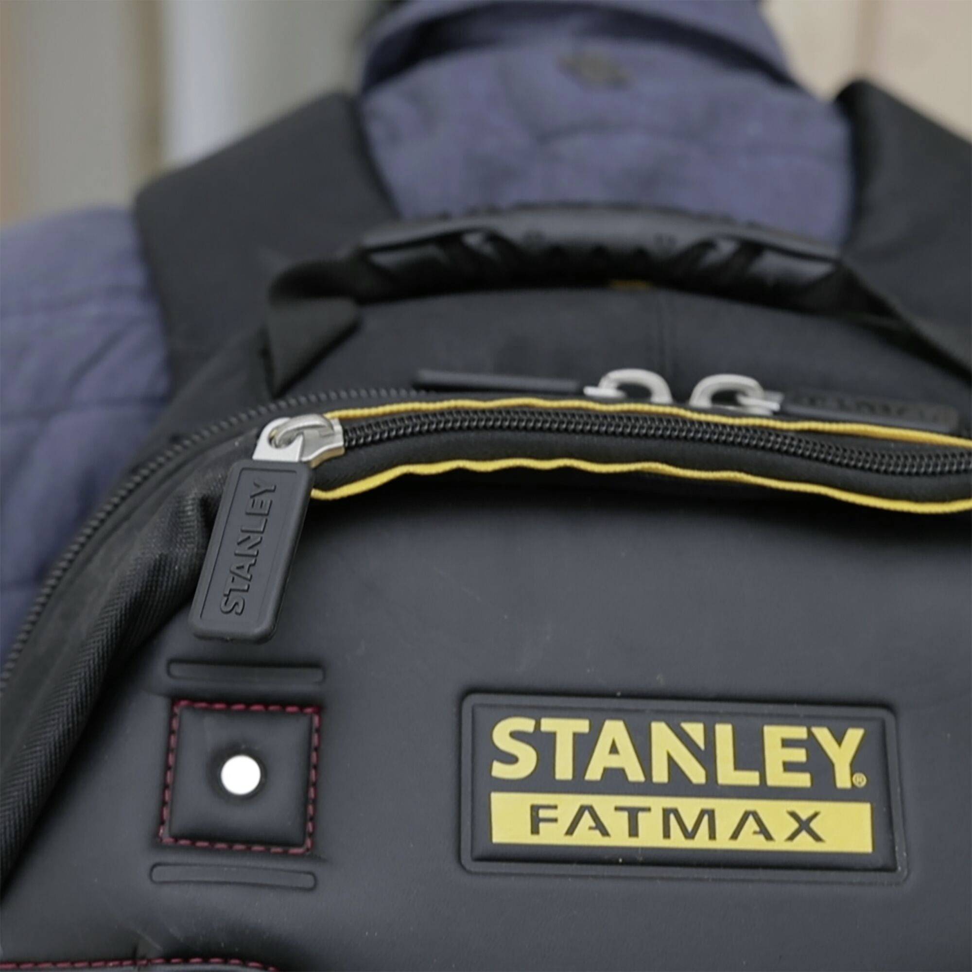 Černý batoh s žlutým logem 'STANLEY FATMAX'. Zip má přívěsek s nápisem 'STANLEY'.