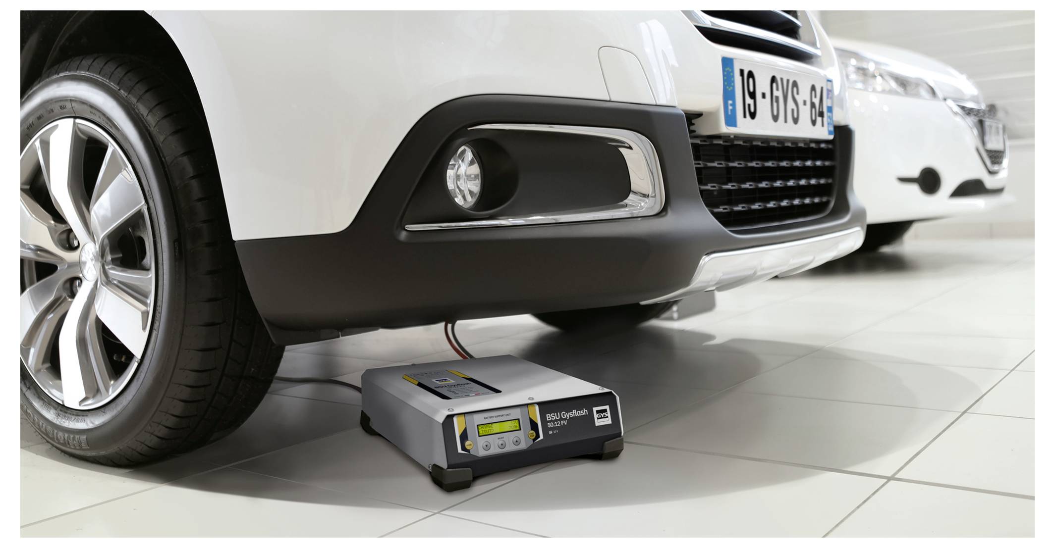 Bílé auto je zaparkováno přes přenosnou nabíječku baterií připojenou pod přední nárazník v garáži nebo v showroomu.