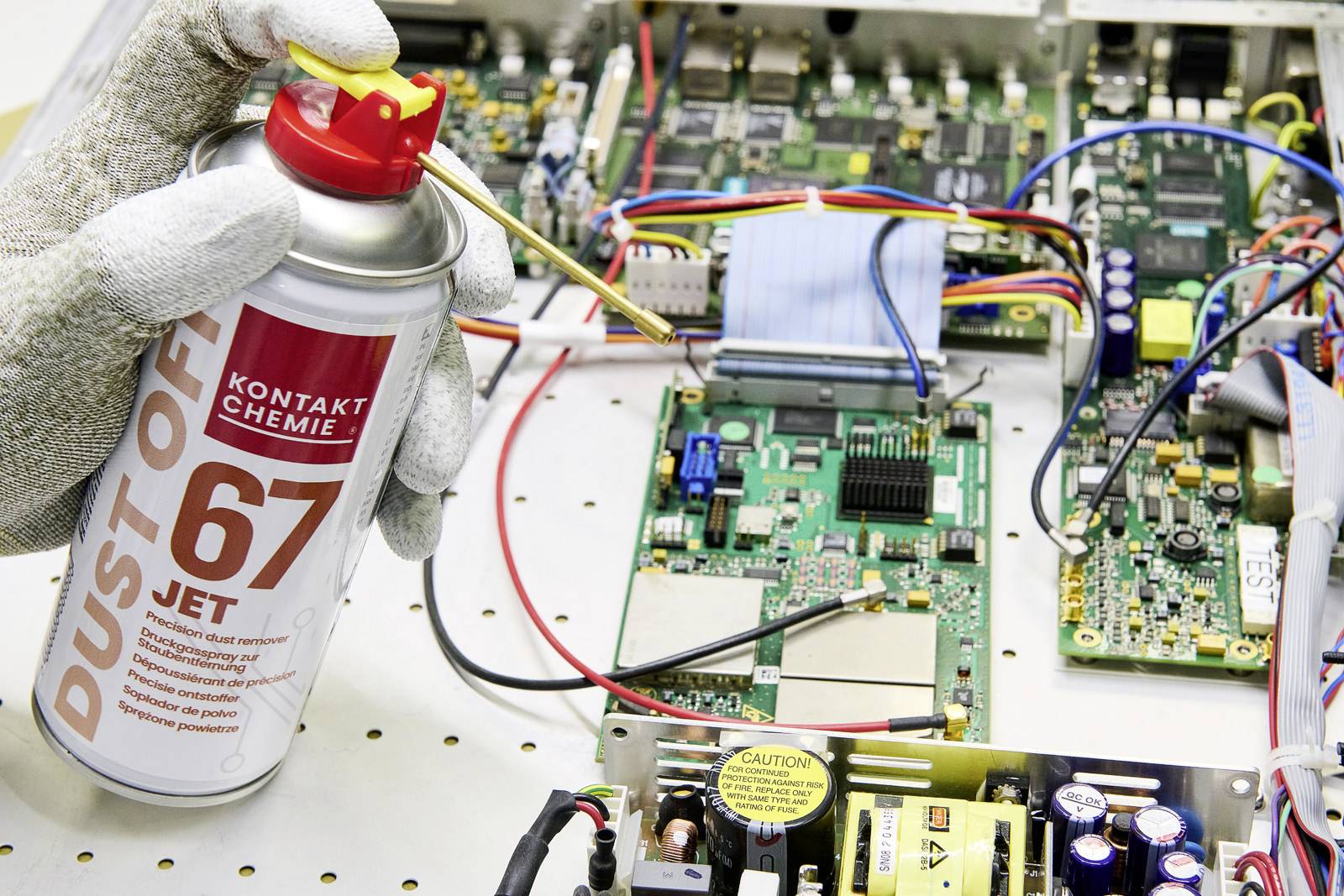 Ruka postřikuje elektronický obvod čisticím sprejem, aby zbavila komponenty prachu.