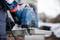 Osoba řeže betonový blok modrou ruční okružní pilou Bosch a pro bezpečnost má na sobě pracovní rukavice.