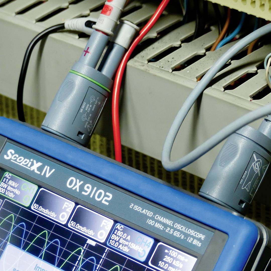 Elektrické měřicí zařízení zobrazuje data z připojených kabelů. Displej obsahuje grafické průběhy vln a numerické hodnoty.