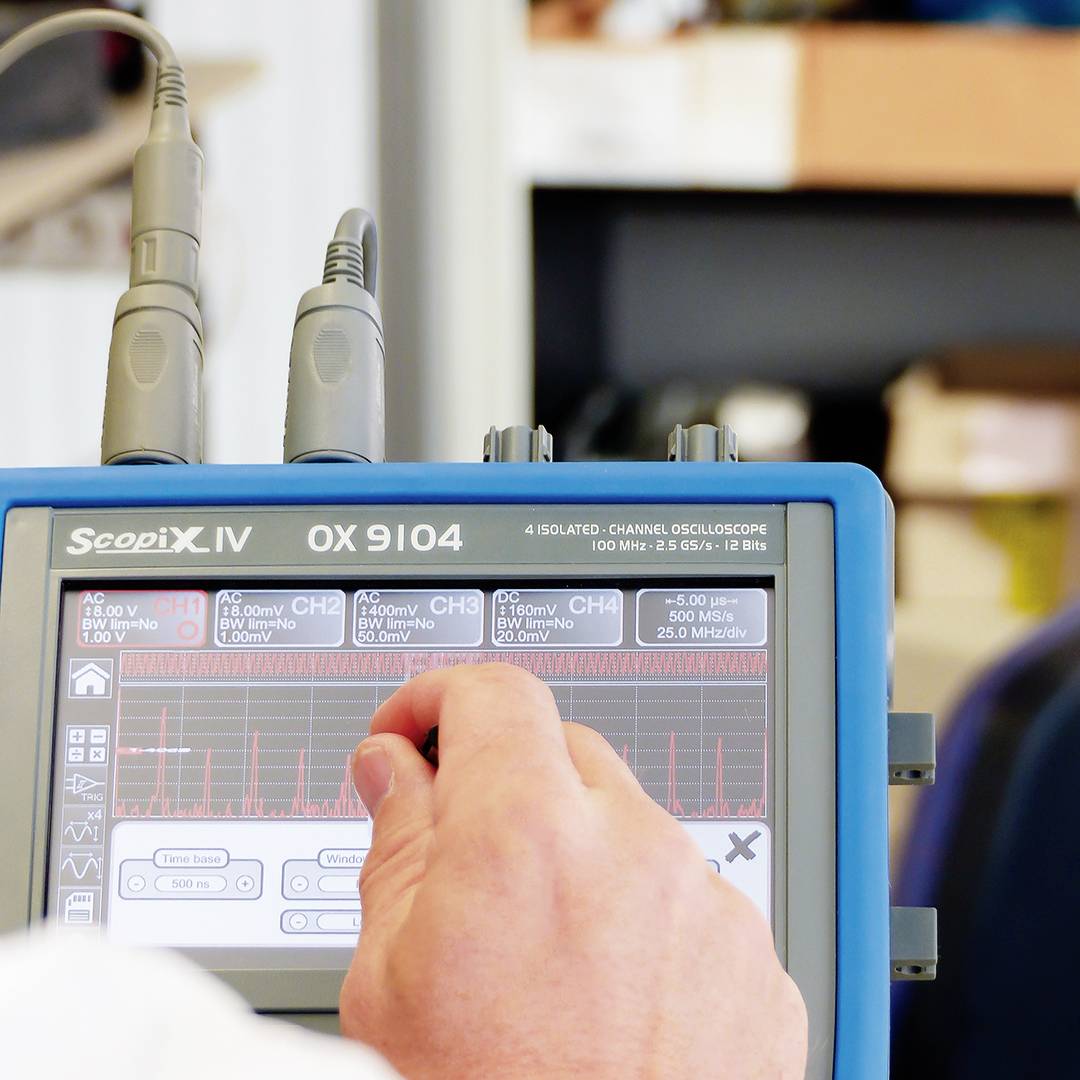 Technik používá osciloskop k měření elektrických signálů. Displej zobrazuje průběhy vln a naměřená data.