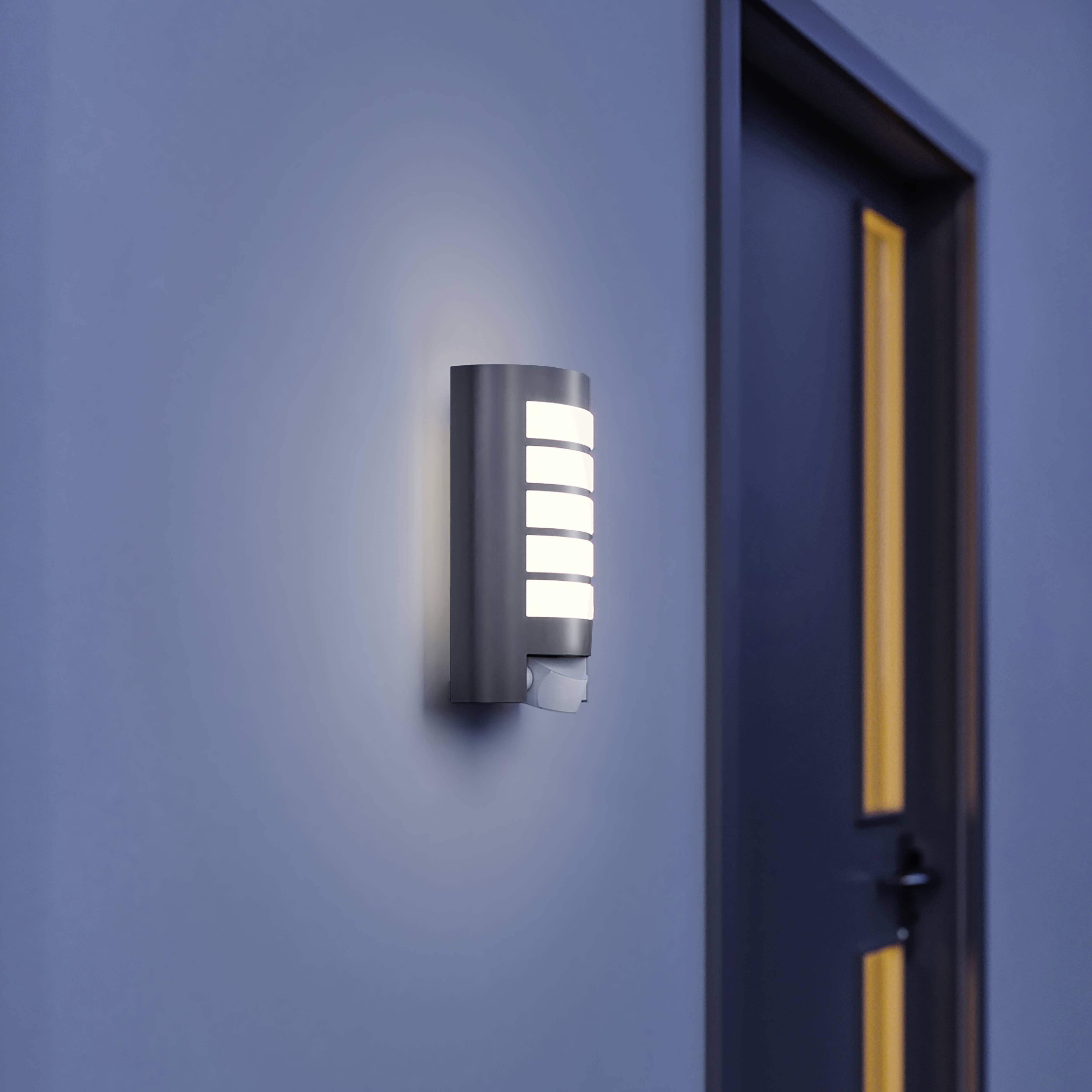 Moderní nástěnná lampa se světlým osvětlením je namontována na šedé stěně vedle dveří, které se nacházejí v moderní budově.