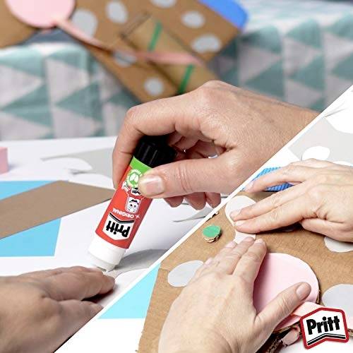 Ruce používající lepicí tyčinku Pritt a připevňující růžový kruhový papírový výřez na kartonový list s řemeslnými materiály v pozadí.