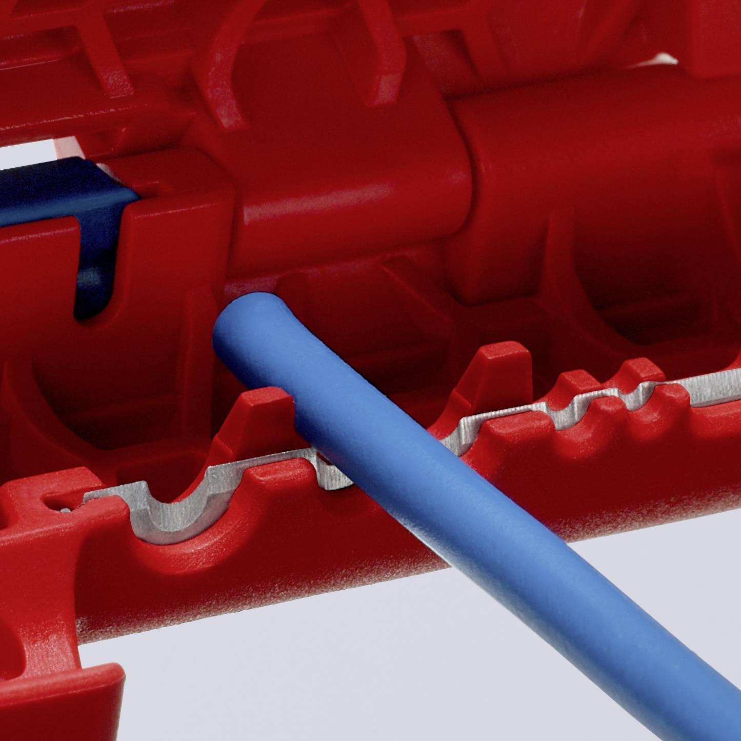 Detailní záběr červeného kabelového kanálu s modrými kabely. Kanál má zubaté hrany a slouží k bezpečnému vedení kabelů.