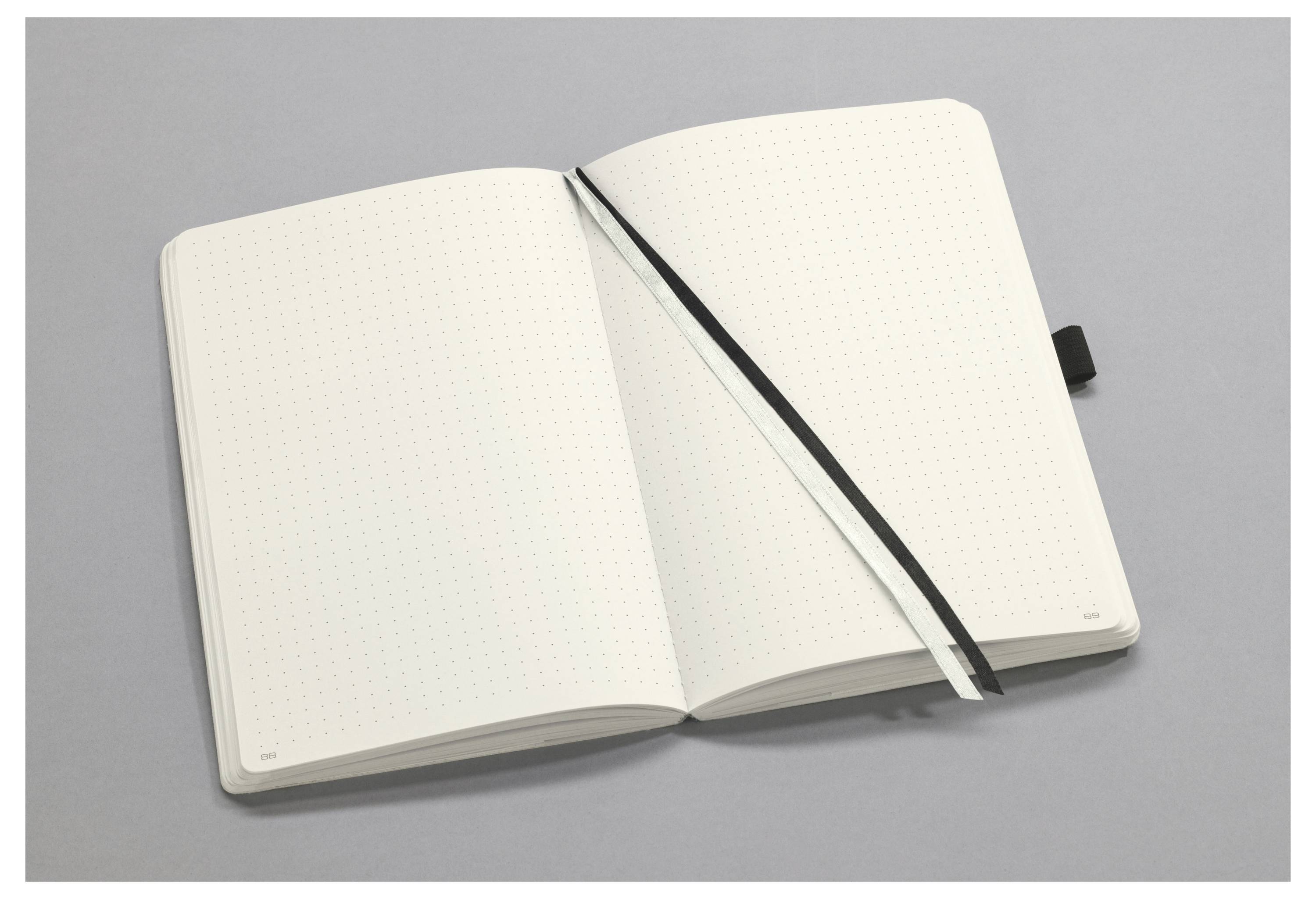 Otevřený prázdný tečkovaný zápisník s černou záložkou na šedém povrchu.