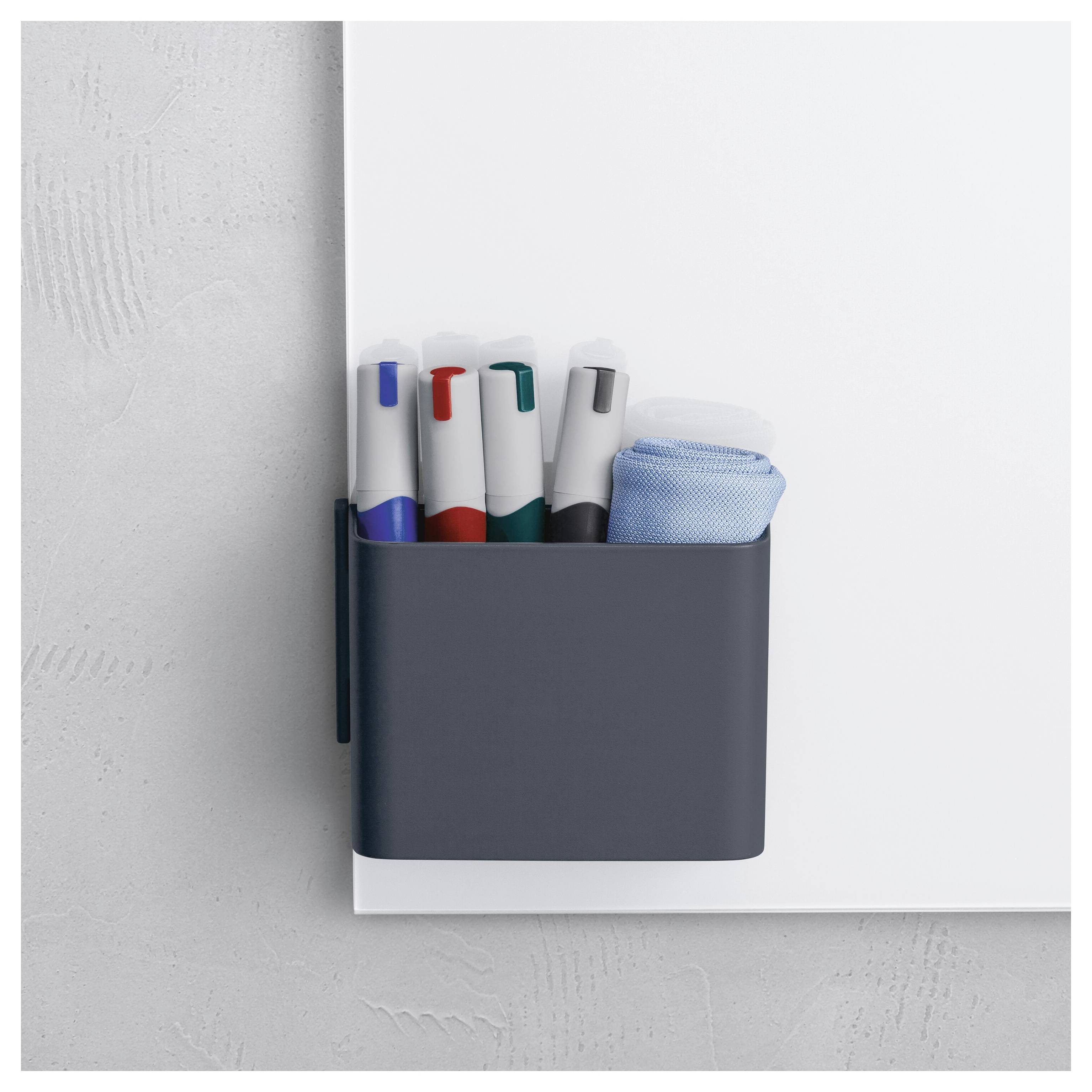 Nástěnný tmavý držák obsahující čtyři značkovače a modrou látku na bílé desce nebo přístroji.