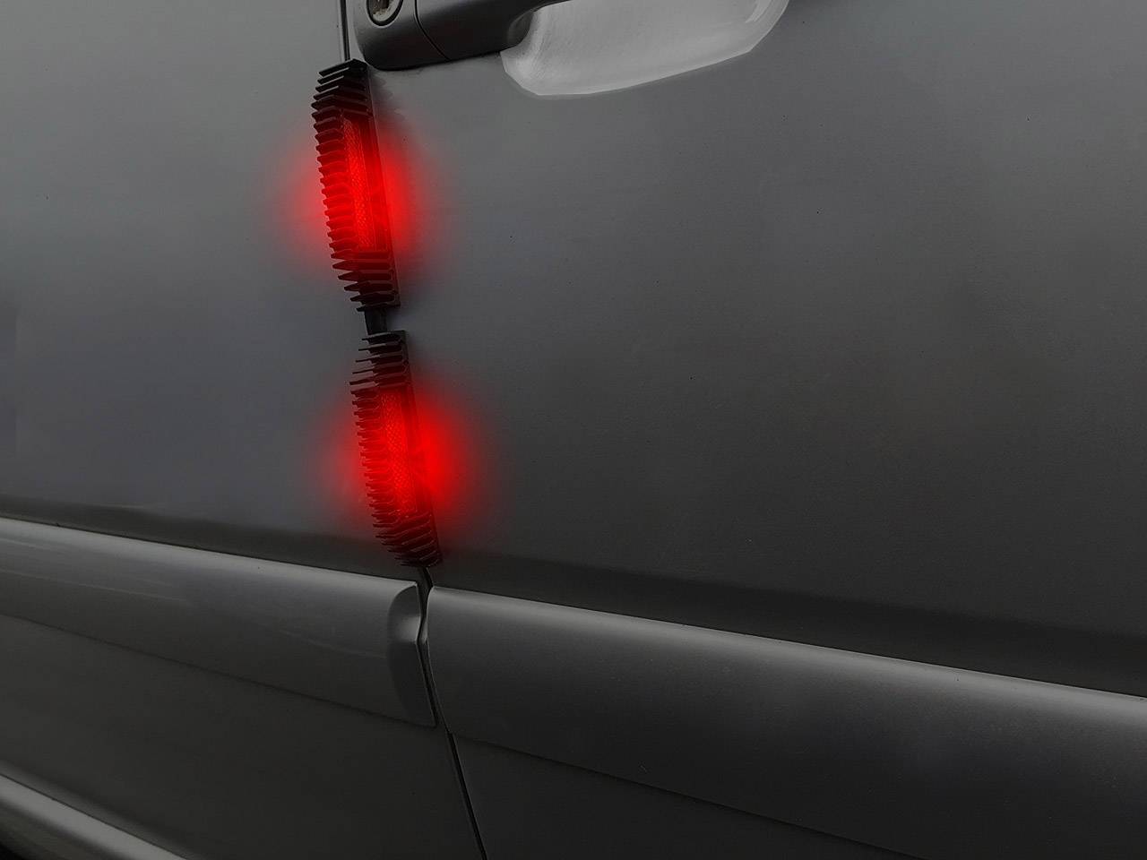 Autosvětlomety ve tmě rudě svítí na hladkém kovovém povrchu, pravděpodobně na automobilu.