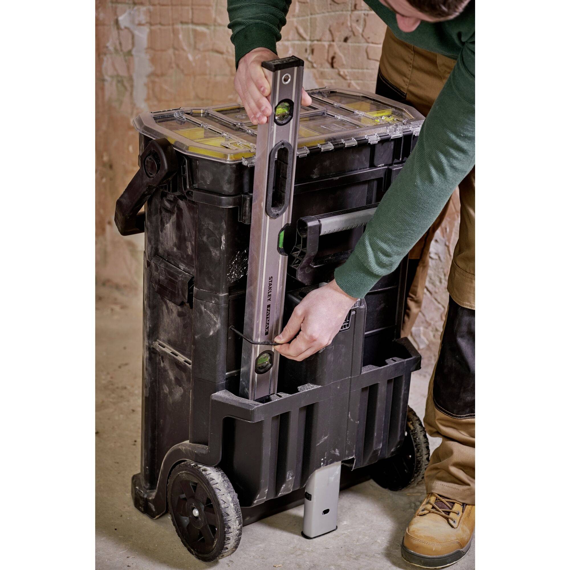 Osoba nastavuje vodováhu na velkém černém pojízdném nářadí v prostředí dílny.