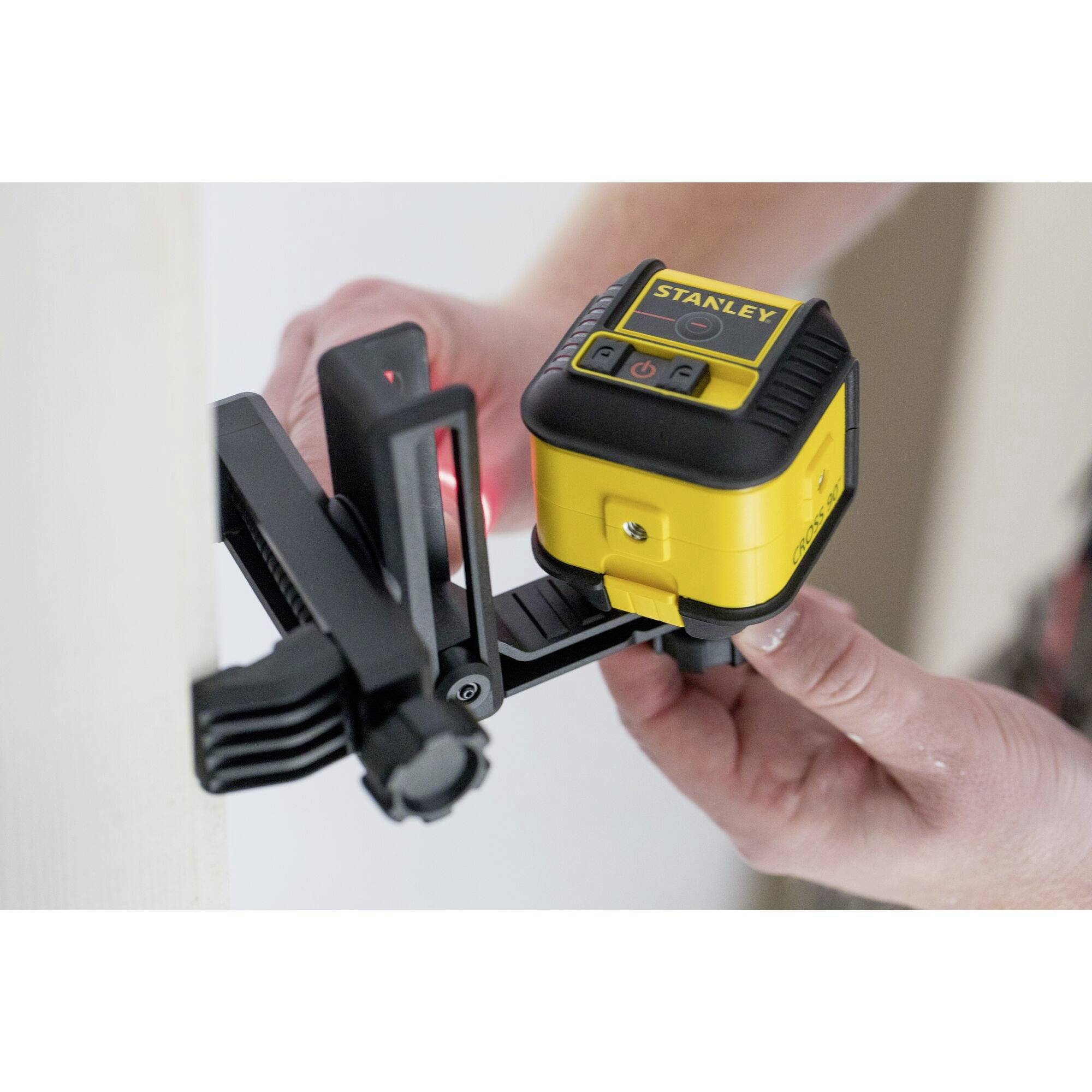 Osoba zaměřuje žluté laserové nivelační zařízení na stěně, které se používá pro stavební nebo DIY práce.