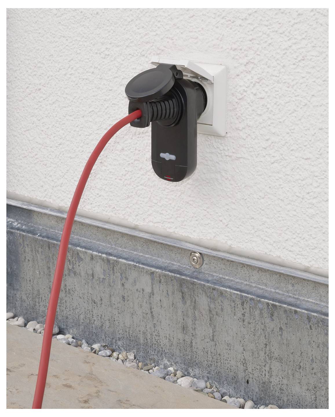 Červený elektrický nabíjecí kabel zapojený do nástěnné nabíjecí zásuvky venku na vnějšku domu.