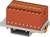 Červený elektrický konektor na šedé základně se žlutými kontakty. Používá se pro propojení elektrických obvodů.