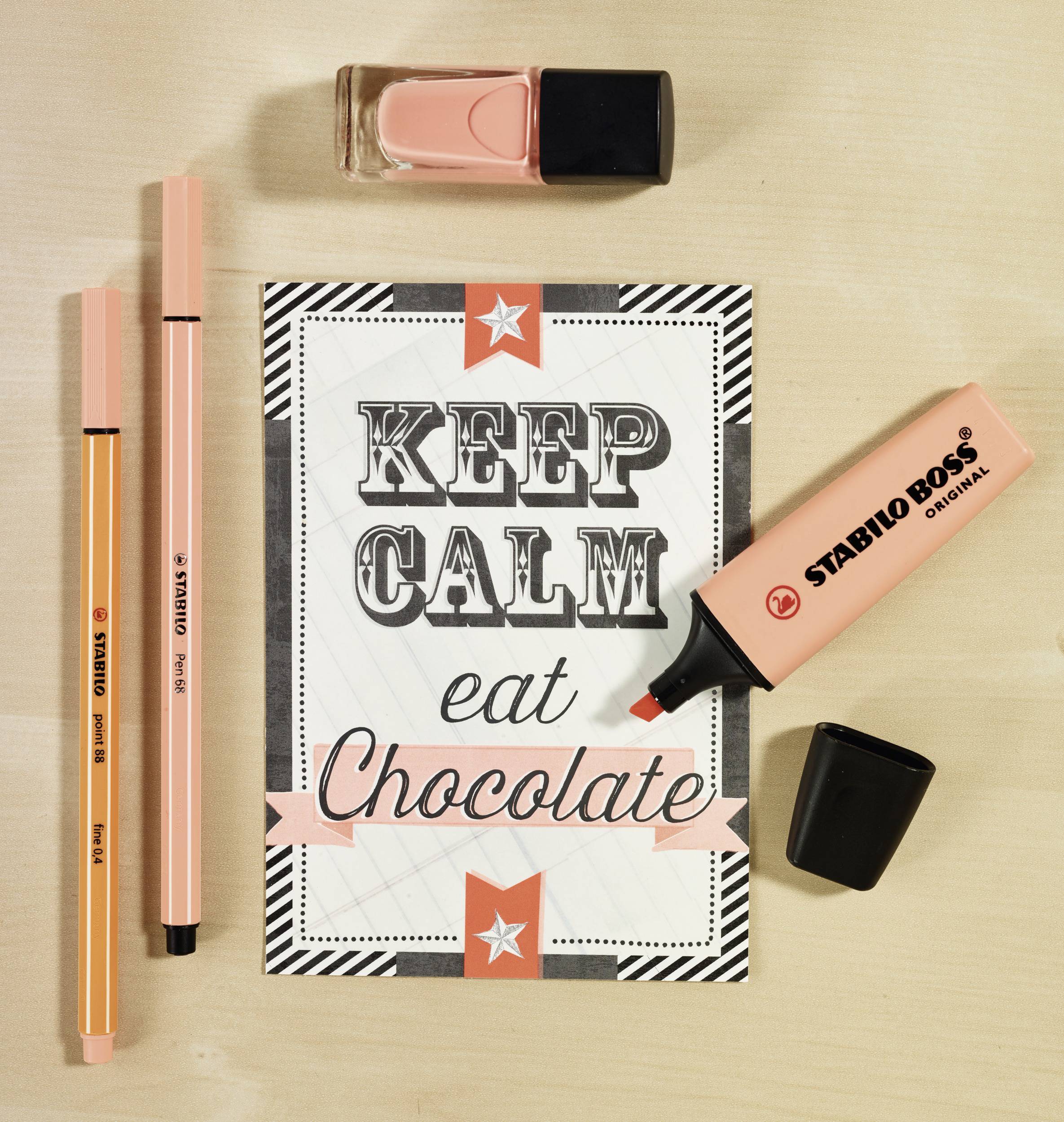 Karta s nápisem 'KEEP CALM jezme Čokoládu' v dekorativním designu, obklopená růžovými tužkami, fixkami a lakem na nehty.